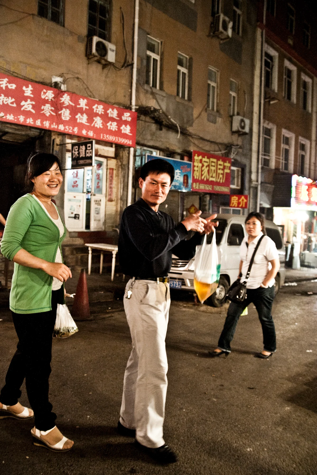 Man carrying bagged draught beer on a street at night, Qingdao — China, documentary and travel photography by Janina Laszlo