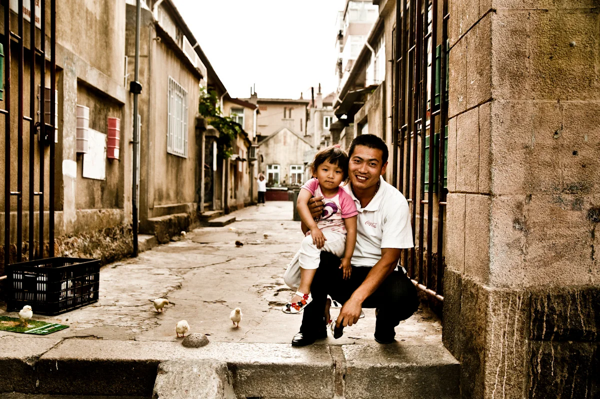 Father and daughter crouching in an old alley with chicks, Qingdao — China, documentary and travel photography by Janina Laszlo