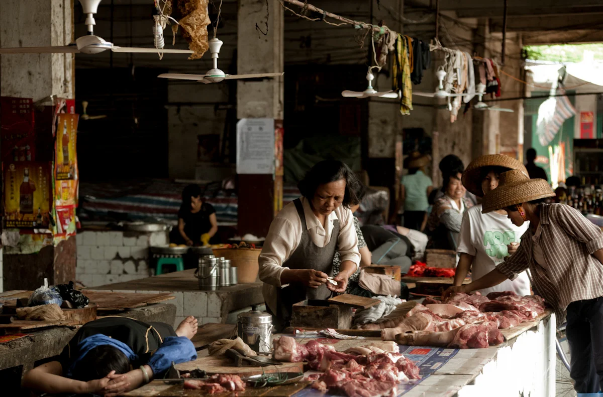 Butcher stall at a covered market with women in straw hats, Hainan — China, documentary and travel photography by Janina Laszlo