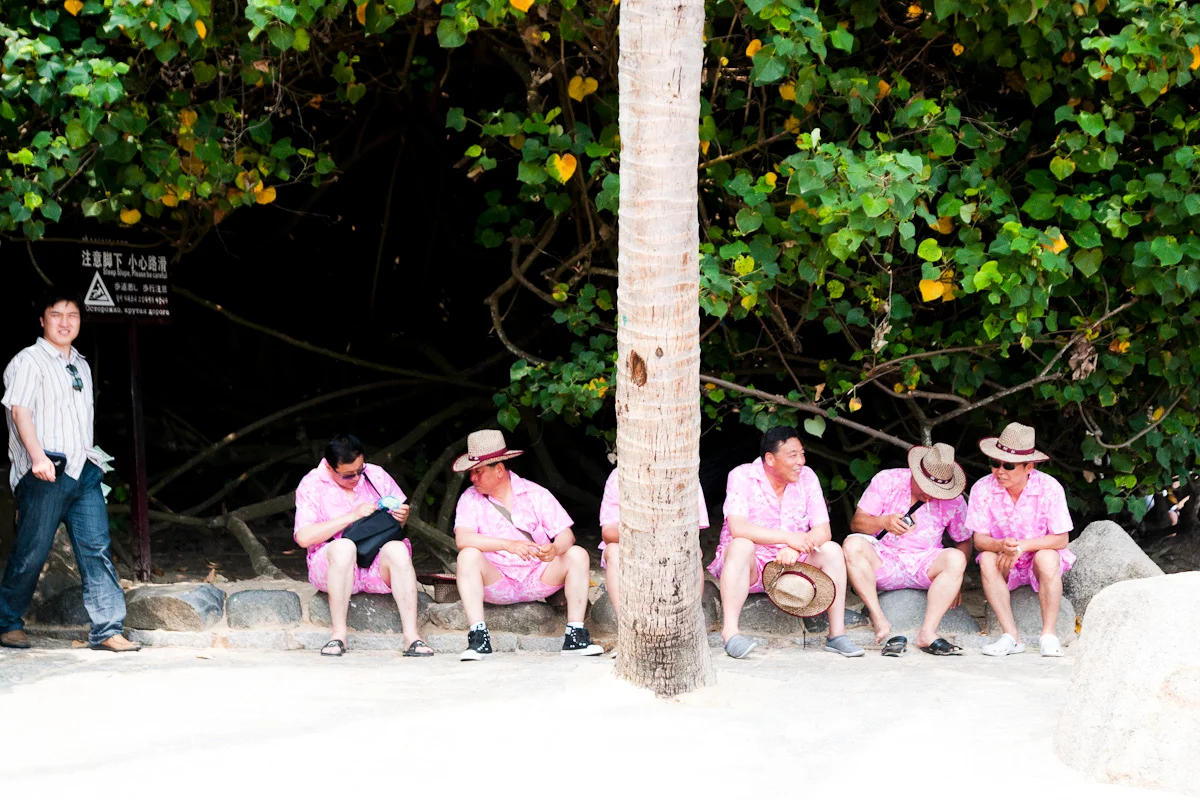 Tourists in matching pink shirts resting under trees on a beach path, Hainan — China, documentary and travel photography by Janina Laszlo