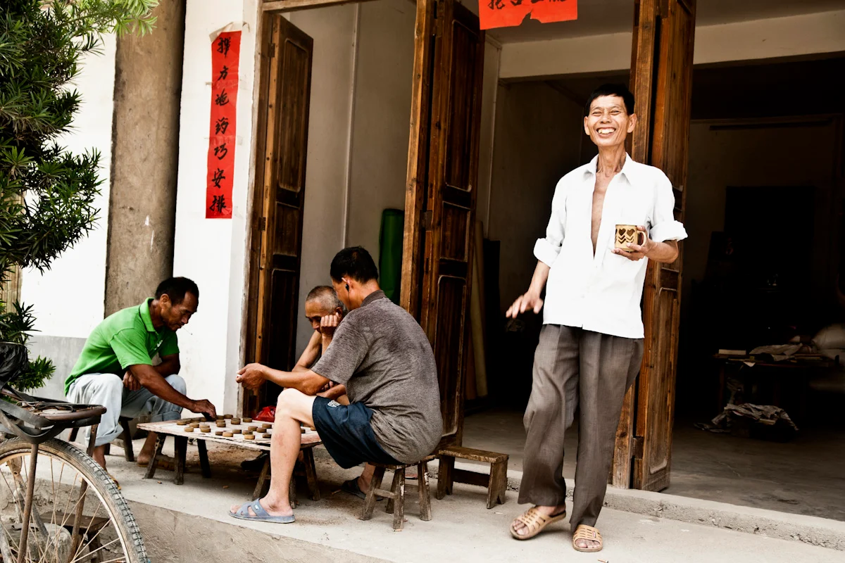Men playing xiangqi (Chinese chess) outside an open shop door — China, documentary and travel photography by Janina Laszlo