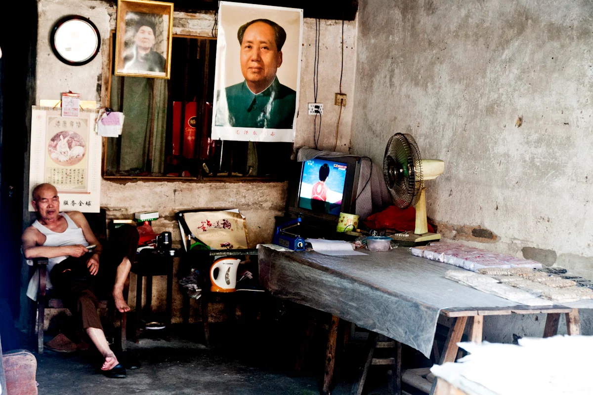 Man resting in a room beneath a portrait of Mao Zedong and a television — China, documentary and travel photography by Janina Laszlo