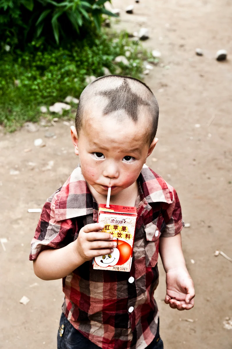 Small boy with a juice carton on a dirt path — China, documentary and travel photography by Janina Laszlo