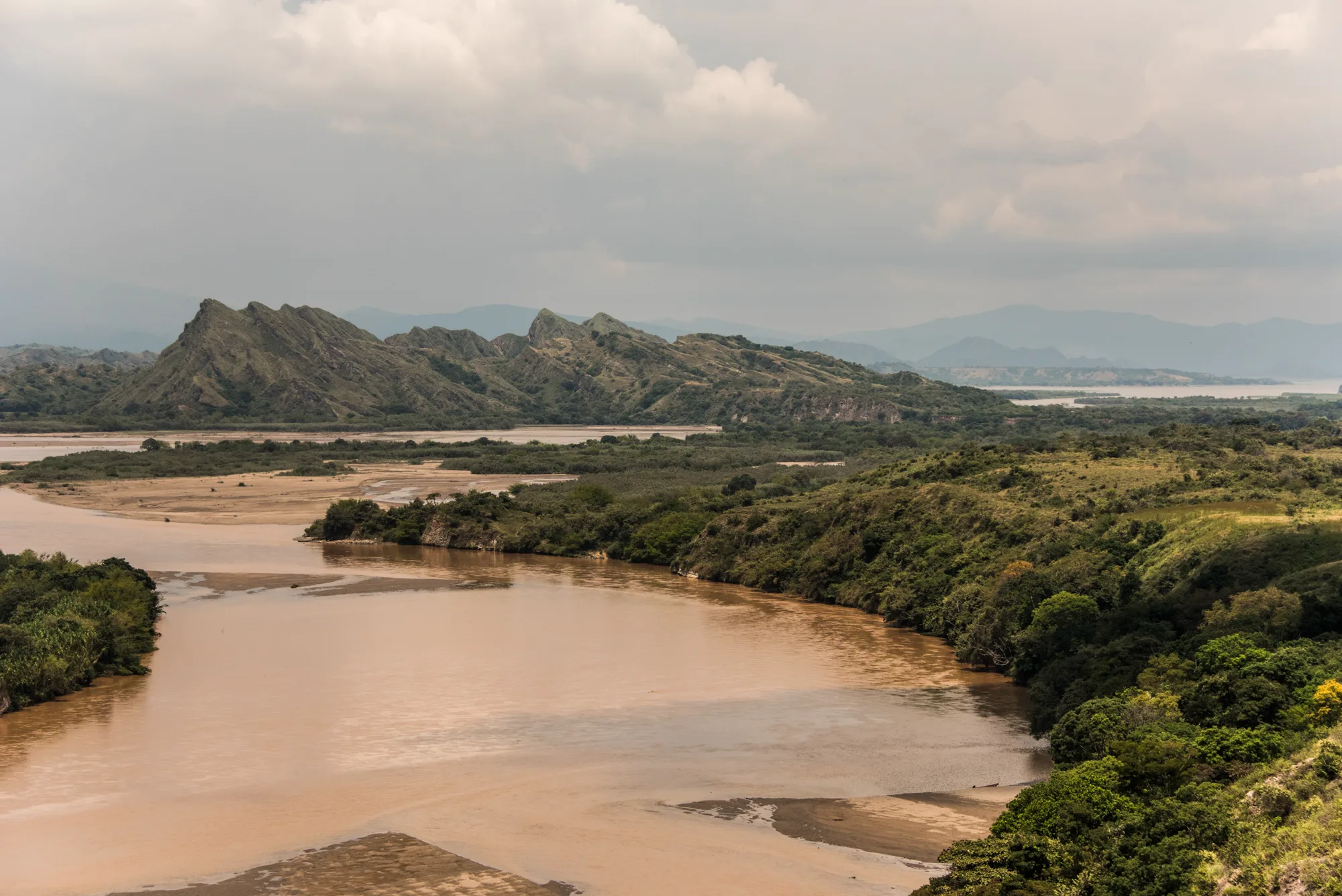 Wide brown river winding between green hills and jagged ridges — Colombia, travel and documentary photography by Janina Laszlo