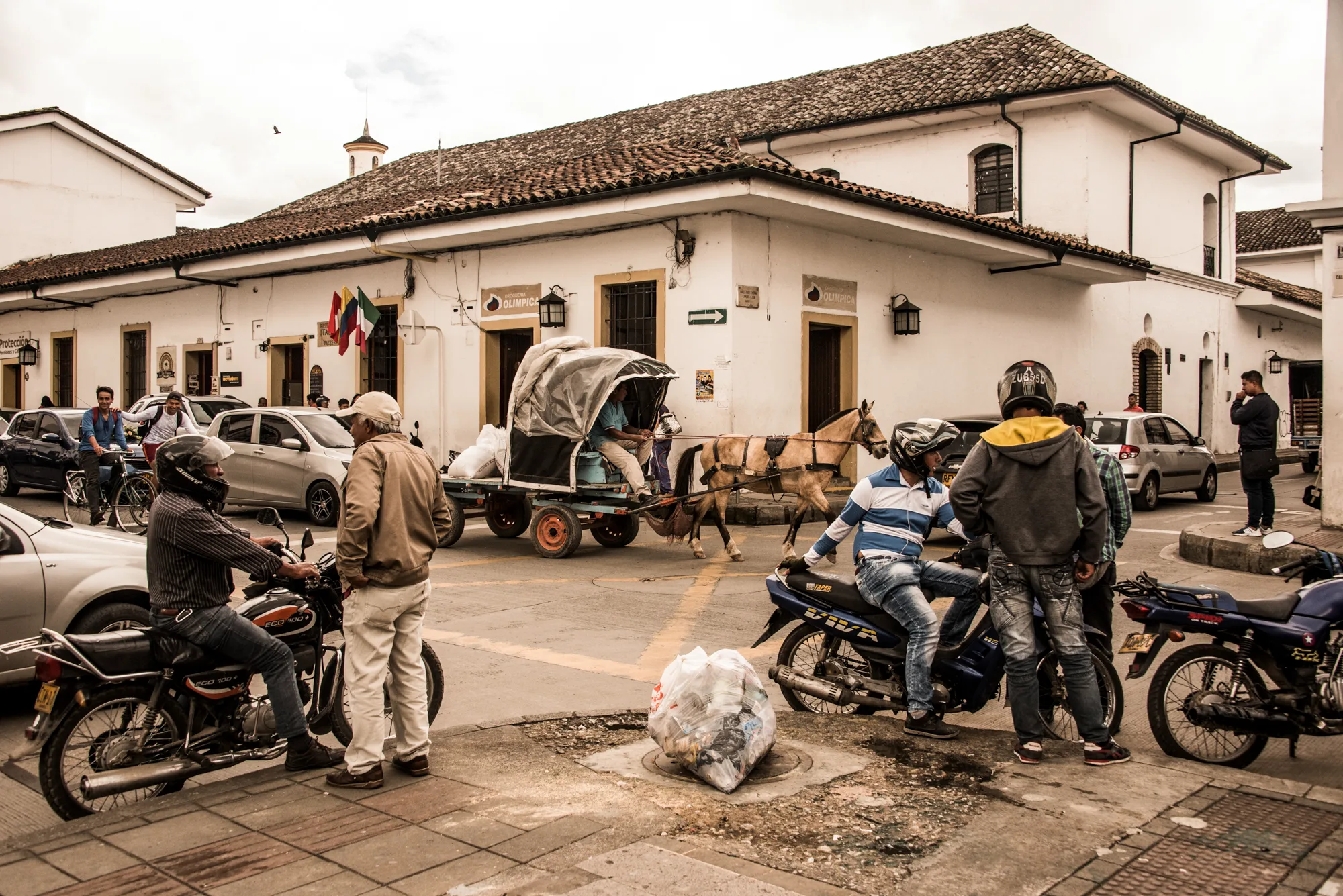 Horse-drawn cart and motorcyclists at a corner of white colonial houses, Popayán — Colombia, travel and documentary photography by Janina Laszlo