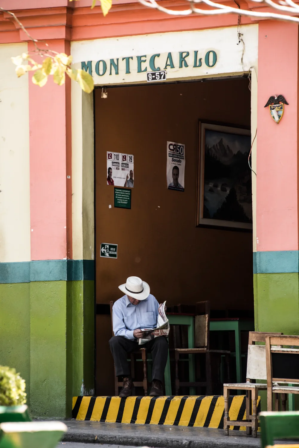 Man in a white hat reading a newspaper in the doorway of a pink-and-green café — Colombia, travel and documentary photography by Janina Laszlo