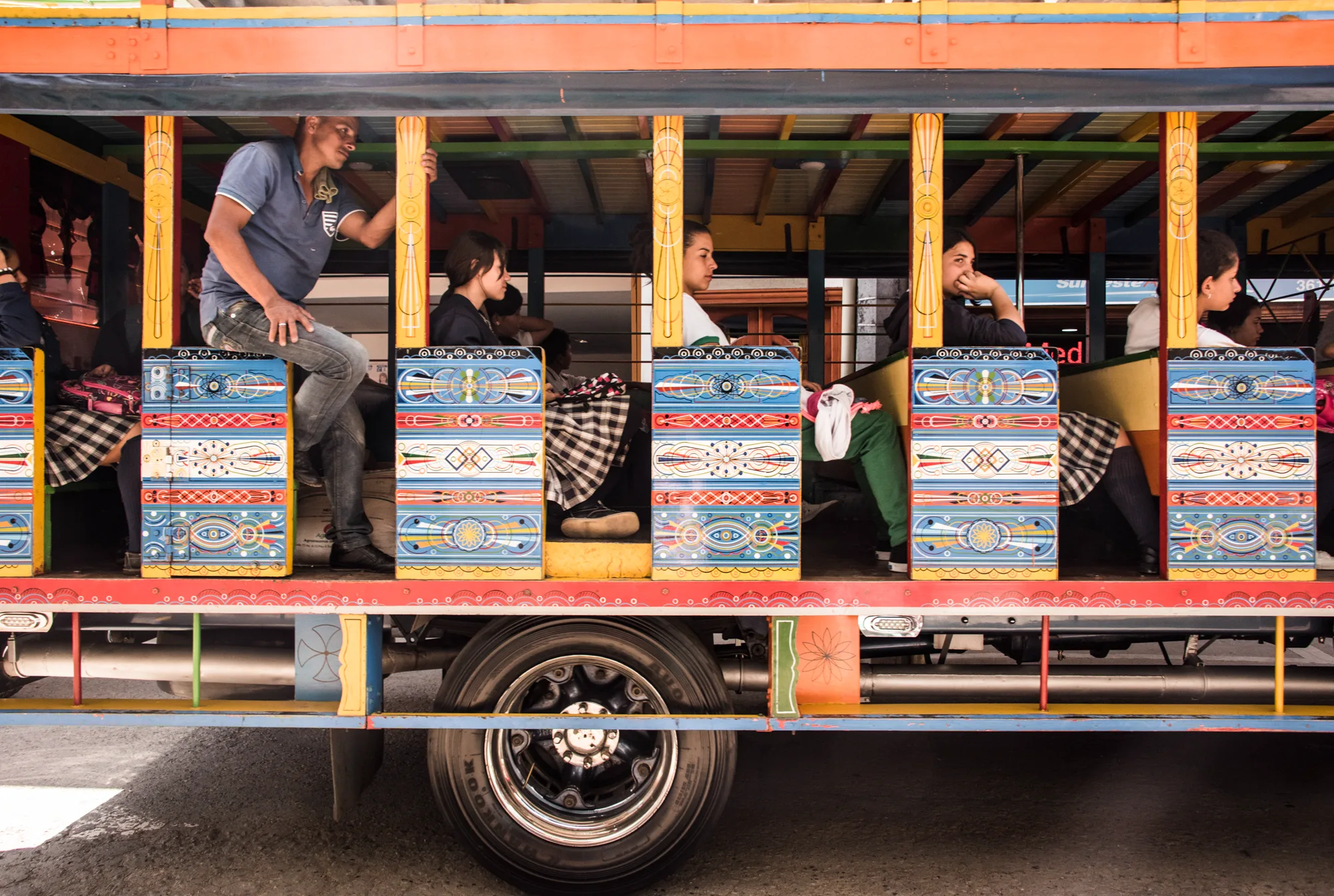 Schoolgirls and a man riding a colourfully painted chiva bus, Antioquia — Colombia, travel and documentary photography by Janina Laszlo