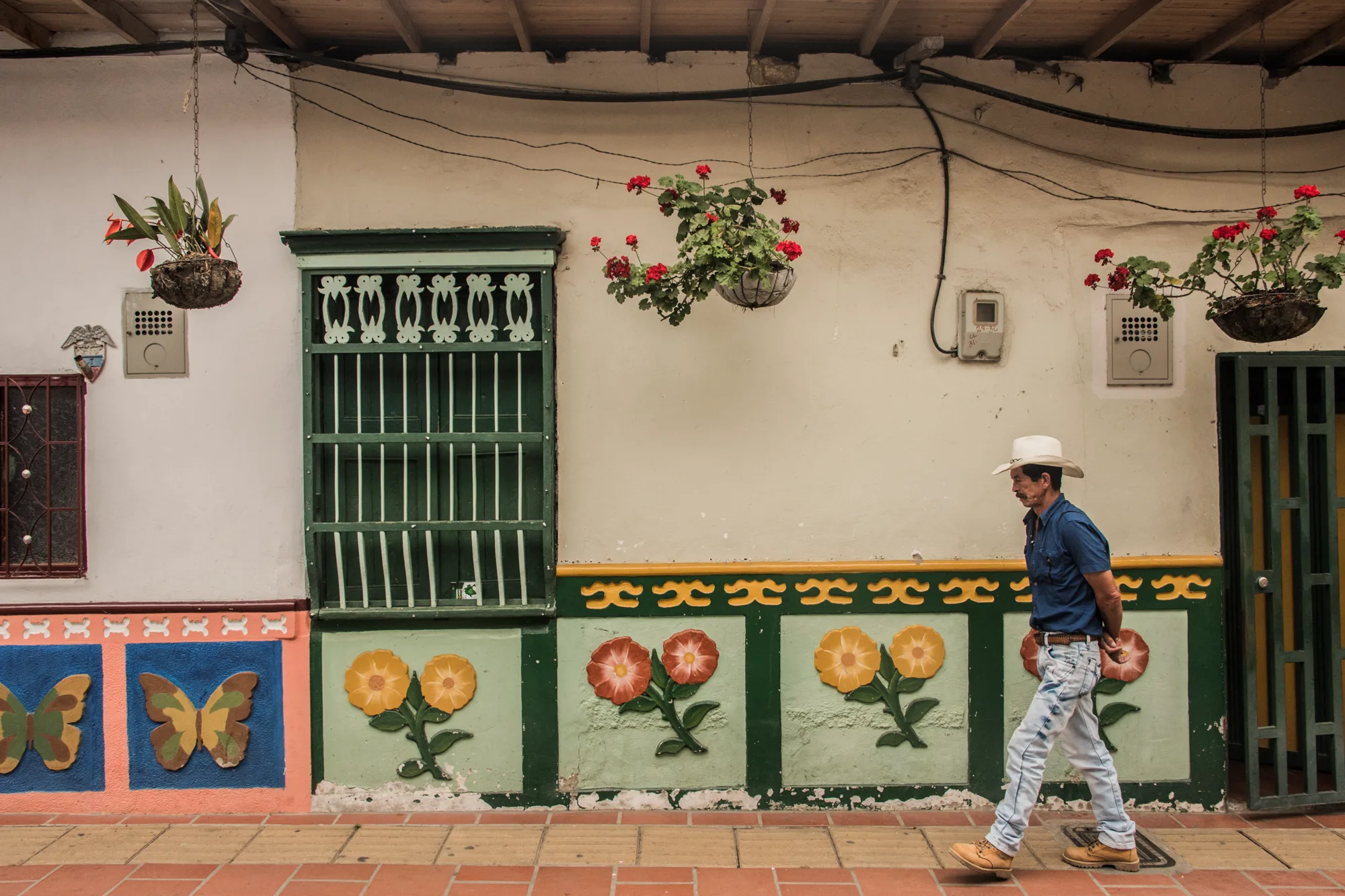 Man in a cowboy hat walking past a facade with relief flowers and butterflies, Guatapé — Colombia, travel and documentary photography by Janina Laszlo