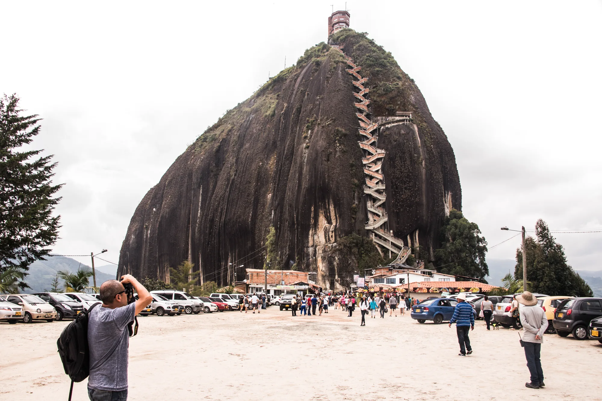 El Peñol de Guatapé monolith with its zigzag staircase above a crowded car park — Colombia, travel and documentary photography by Janina Laszlo