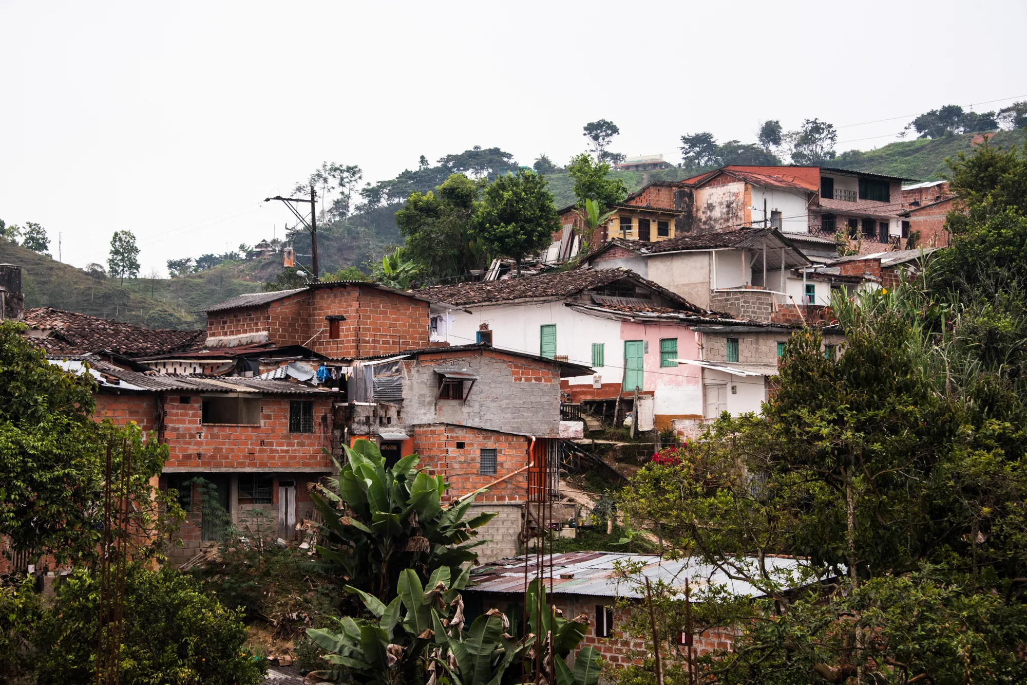 Brick and white houses stacked on a green hillside — Colombia, travel and documentary photography by Janina Laszlo