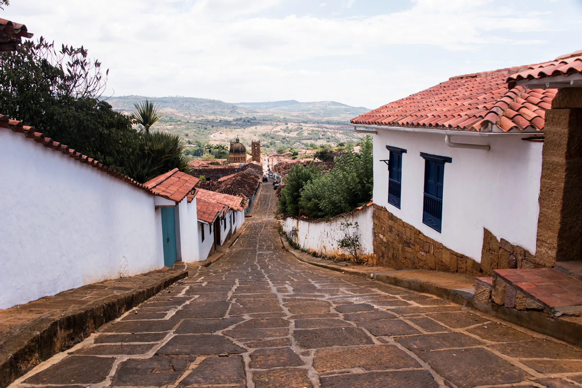 Sloping stone-paved street of white houses with red-tiled roofs leading to the cathedral, Barichara — Colombia, travel and documentary photography by Janina Laszlo