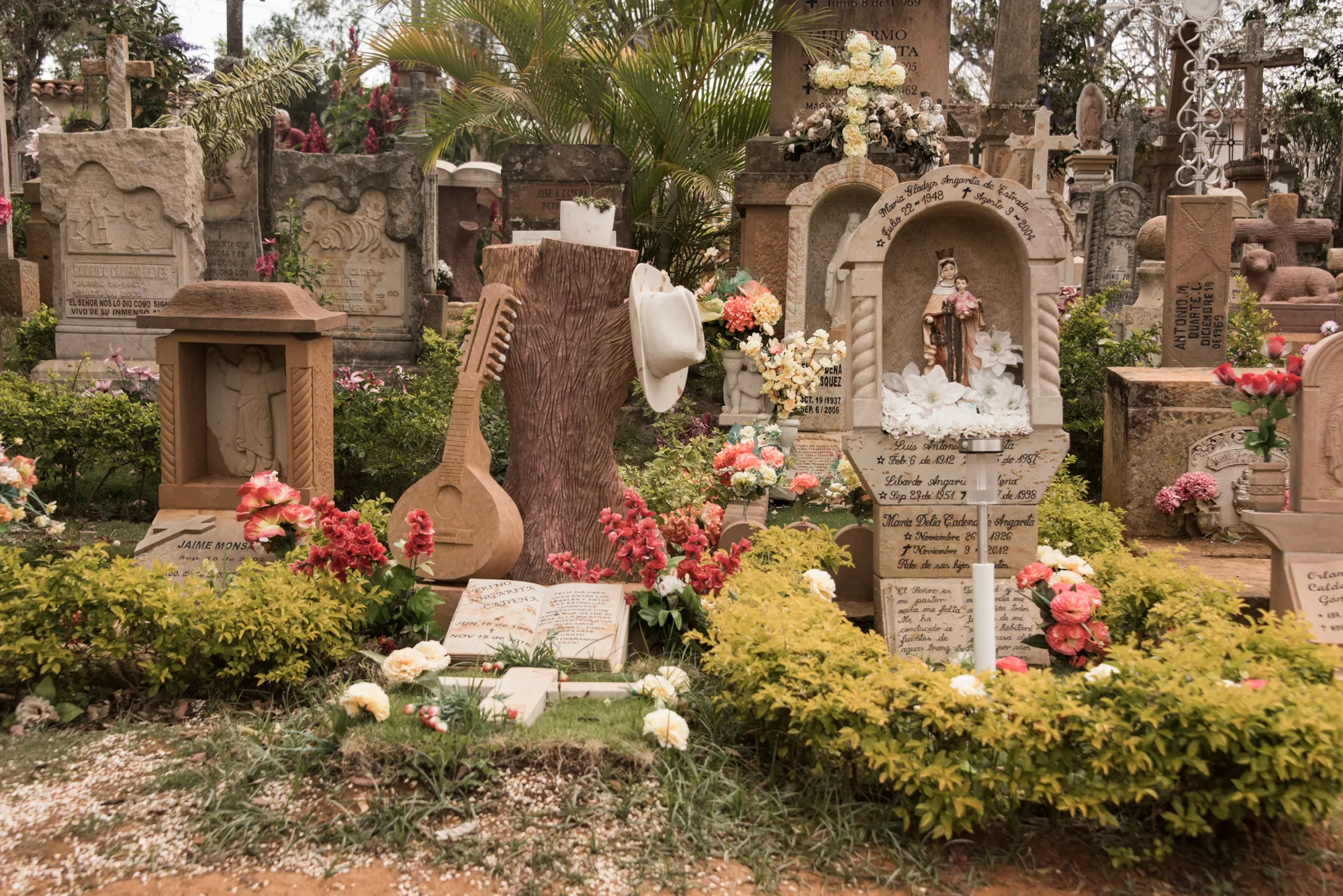 Carved sandstone graves, flowers and a guitar sculpture in the cemetery of Barichara — Colombia, travel and documentary photography by Janina Laszlo