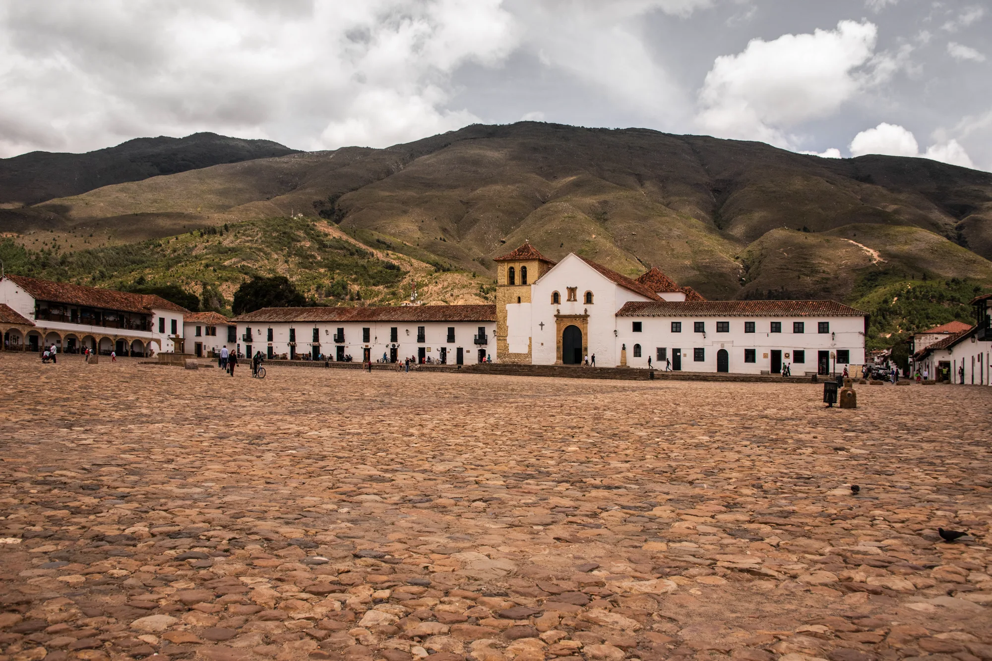 Vast cobblestone Plaza Mayor with the white parish church below green mountains, Villa de Leyva — Colombia, travel and documentary photography by Janina Laszlo