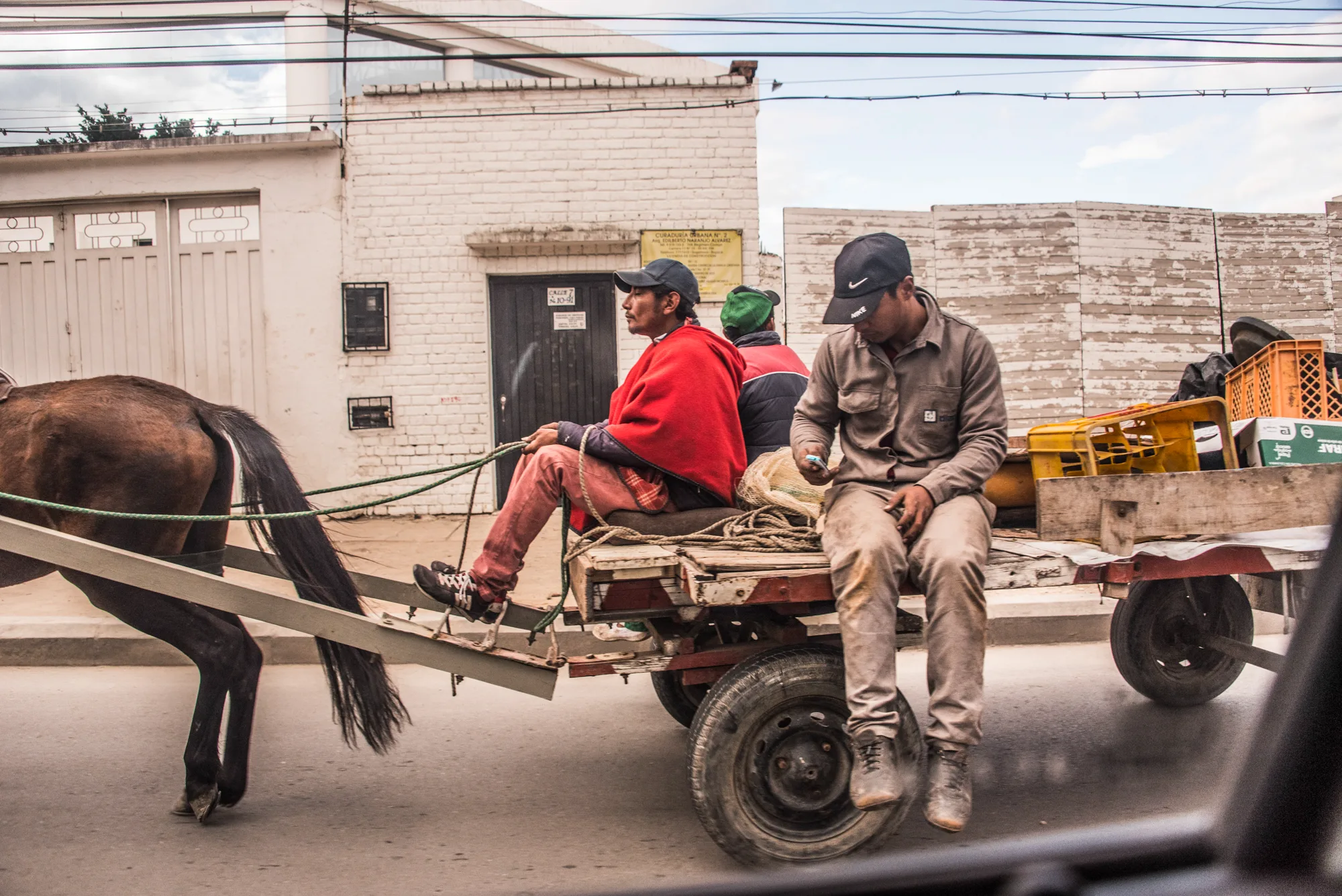 Men riding a horse-drawn cart loaded with crates through town — Colombia, travel and documentary photography by Janina Laszlo