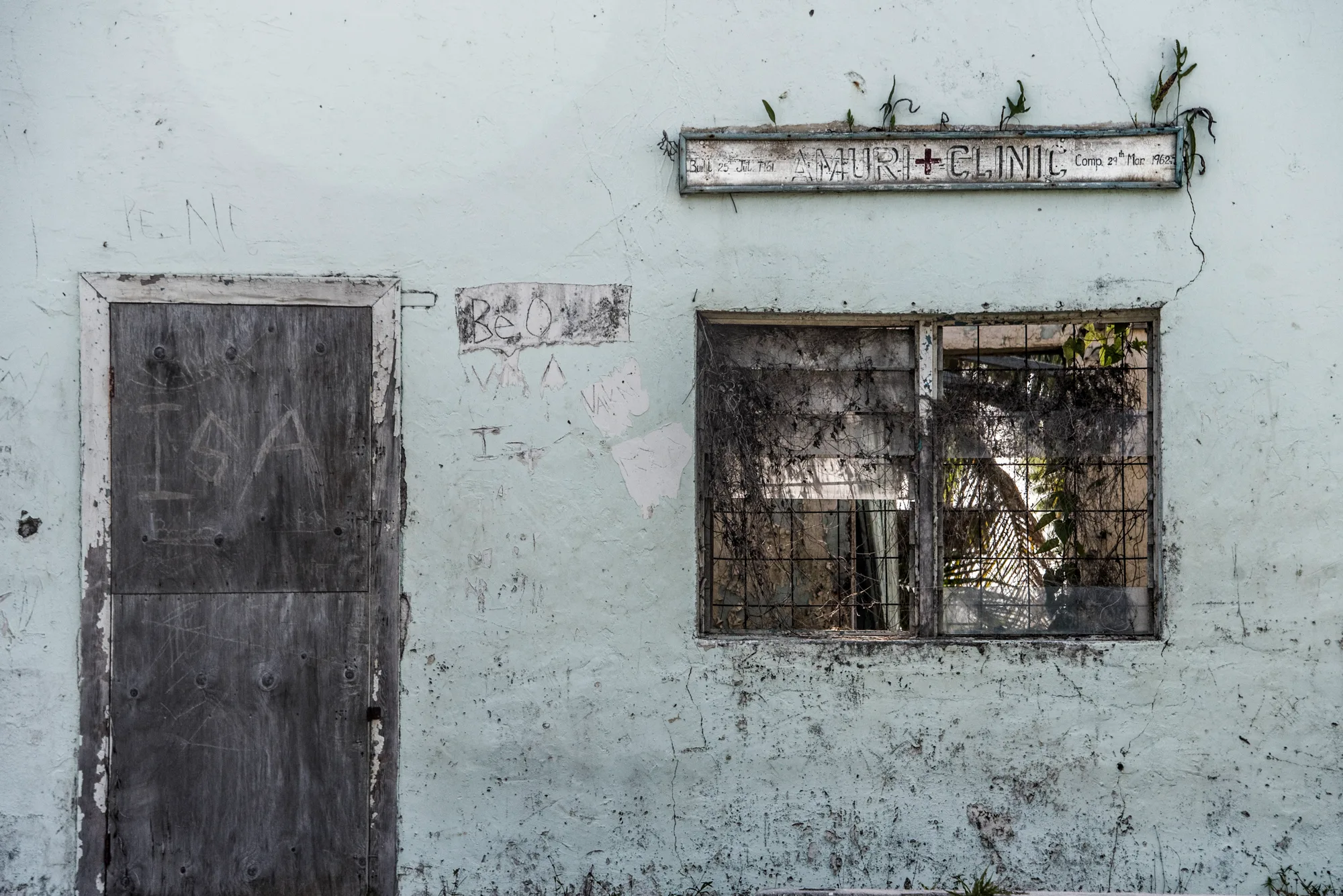 Weathered wall of the Amuri Clinic with a boarded door, Aitutaki — Cook Islands, travel and fine art photography by Janina Laszlo