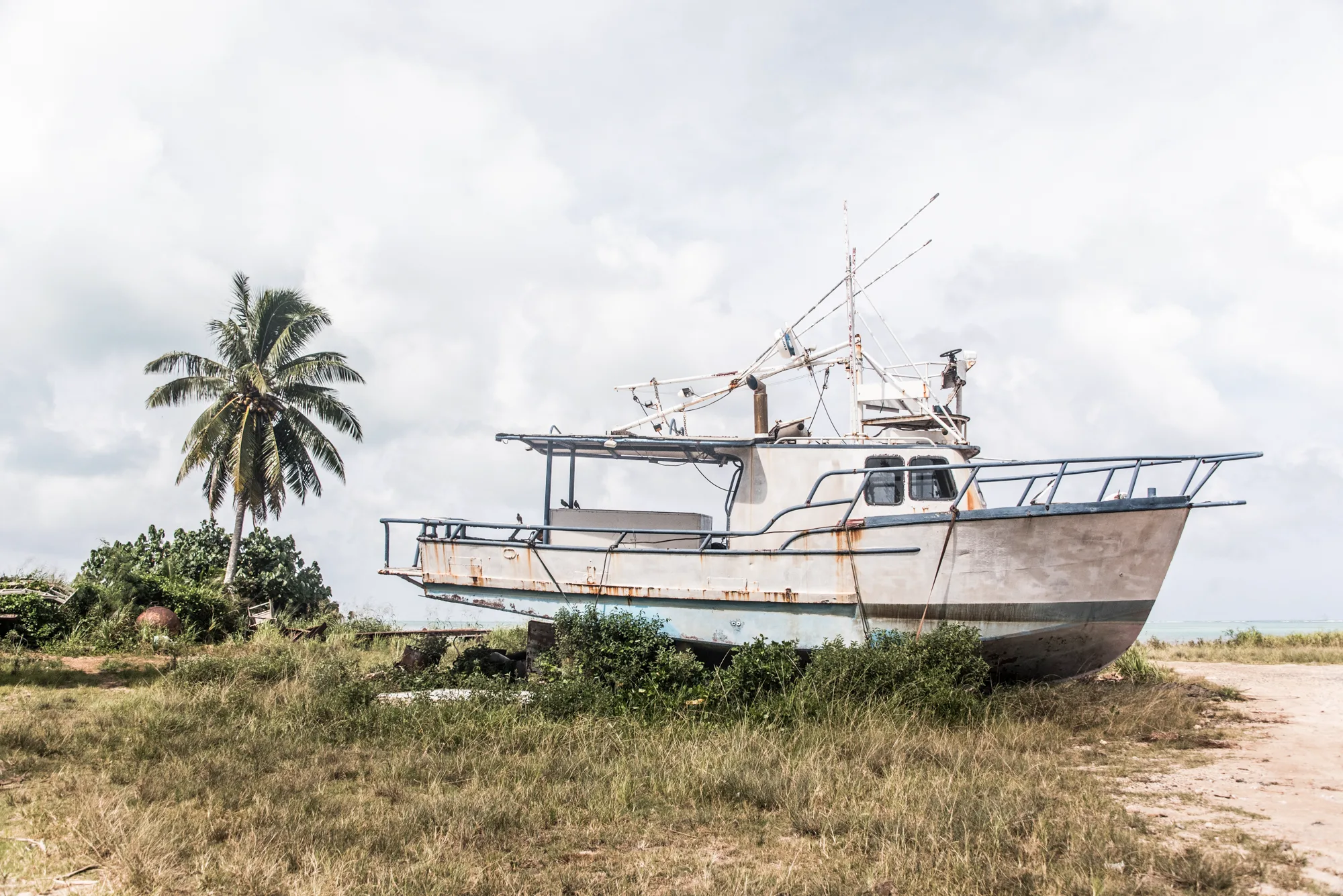 Rusting fishing boat stranded in the grass near the shore — Cook Islands, travel and fine art photography by Janina Laszlo
