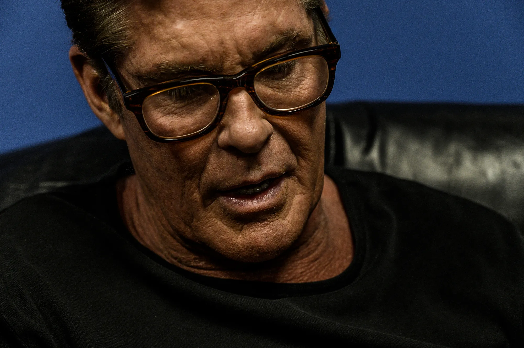 David Hasselhoff in tortoiseshell glasses looking down, close-up backstage against a blue wall — editorial and behind-the-scenes photography during a concert appearance, by German photographer Janina Laszlo