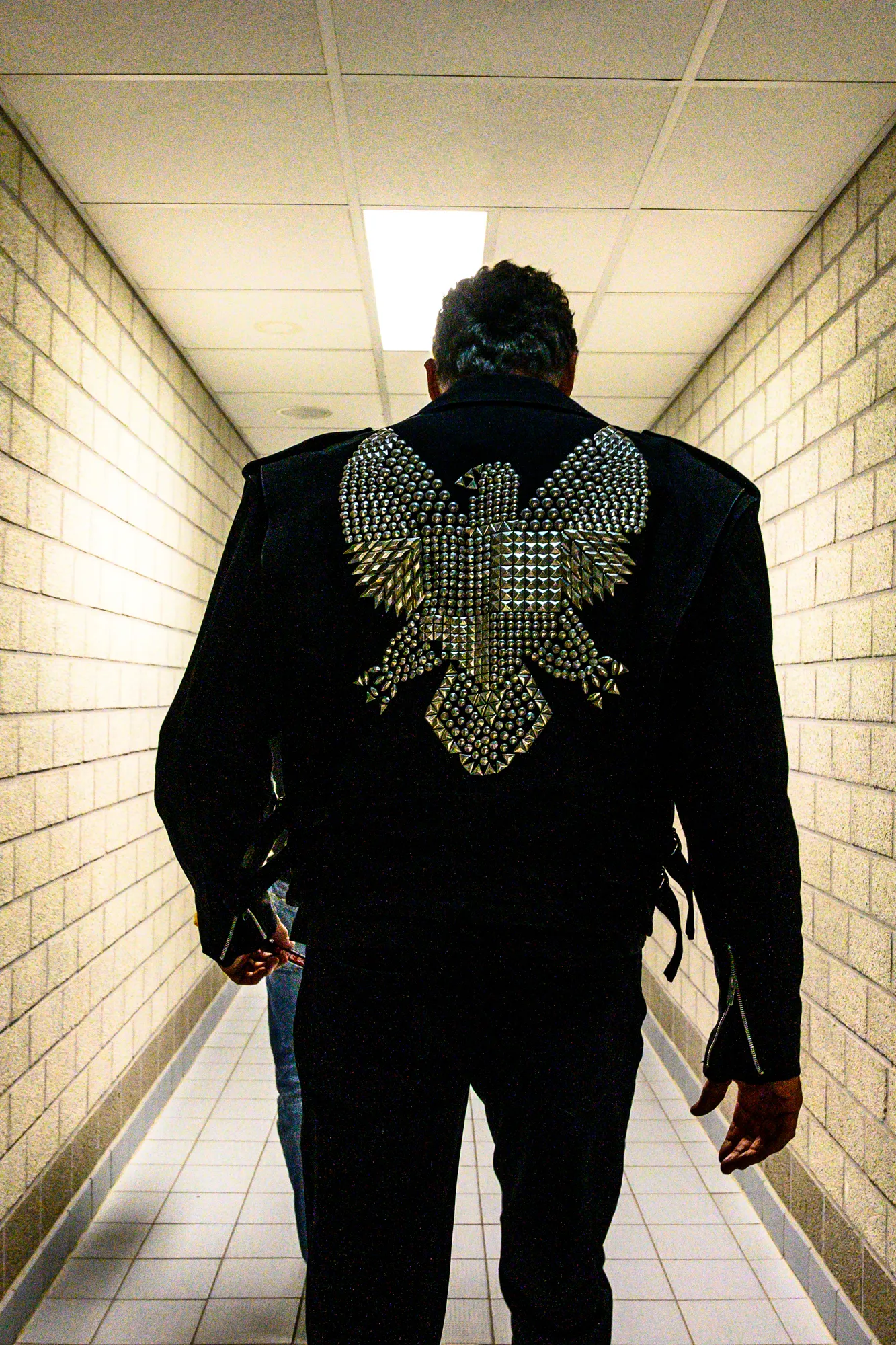 David Hasselhoff seen from behind in a studded eagle leather jacket, walking down a backstage corridor — behind-the-scenes photography by German photographer Janina Laszlo