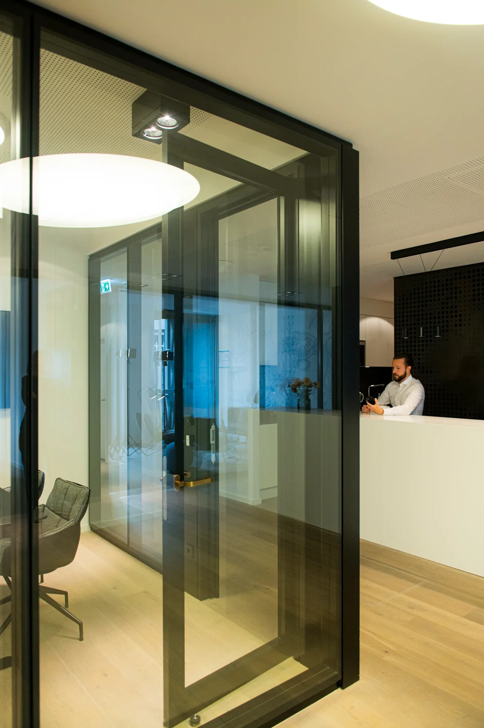 Glass meeting box with black frames in a modern office, colleague at the white counter behind, Frankfurt am Main & Munich — Digital+, corporate photography by Janina Laszlo