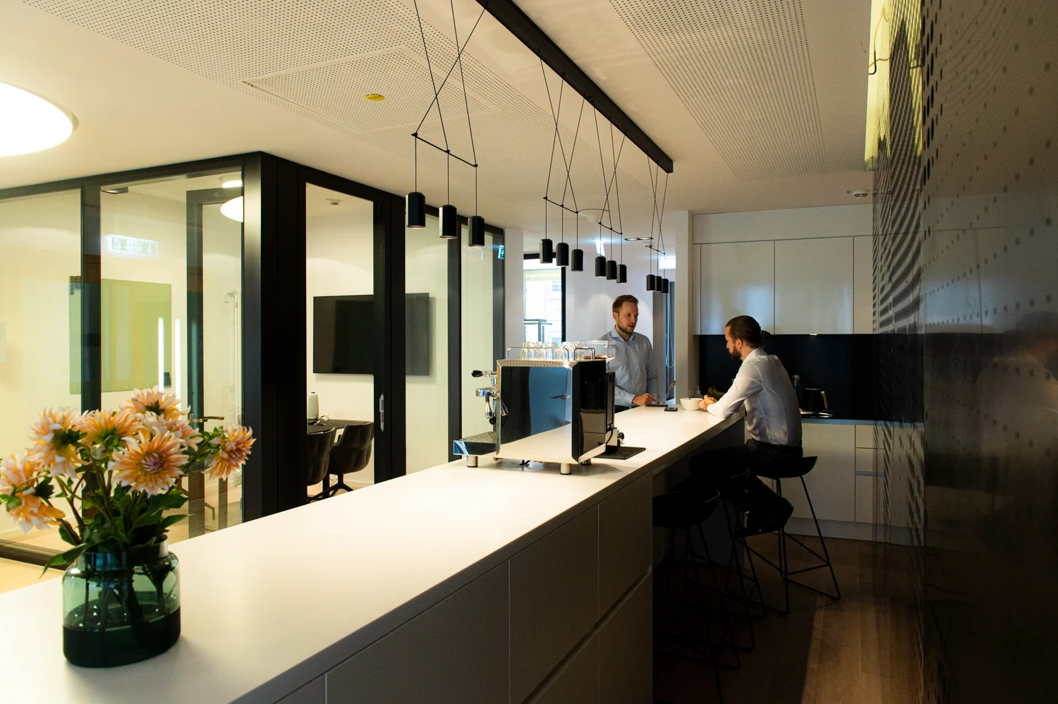 Office coffee bar with pendant lights, espresso machine and two colleagues in conversation, Frankfurt am Main & Munich — Digital+, corporate photography by Janina Laszlo