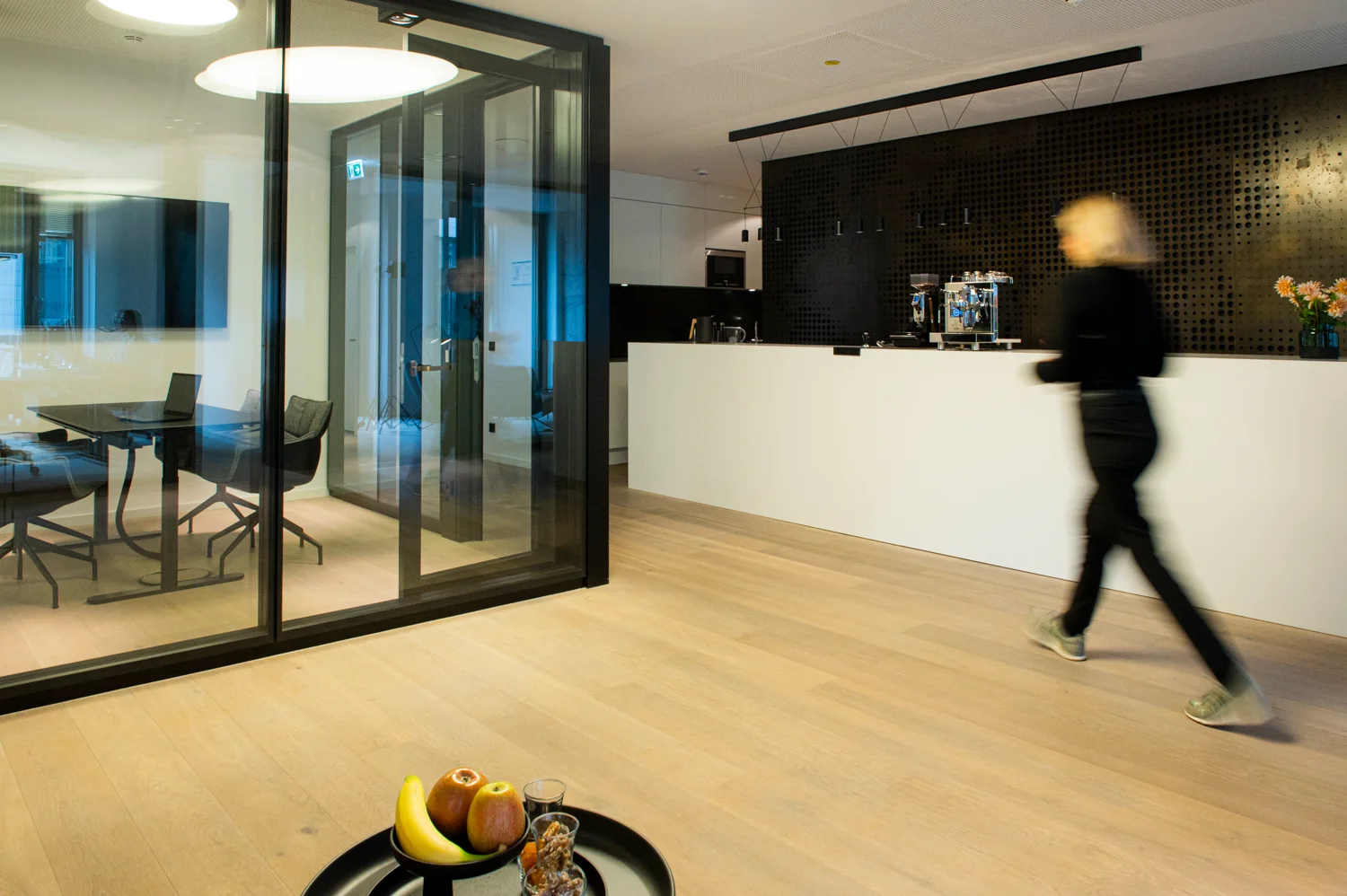 Colleague walking past the white counter and a glass meeting room, motion blur, oak floor, Frankfurt am Main & Munich — Digital+, corporate photography by Janina Laszlo