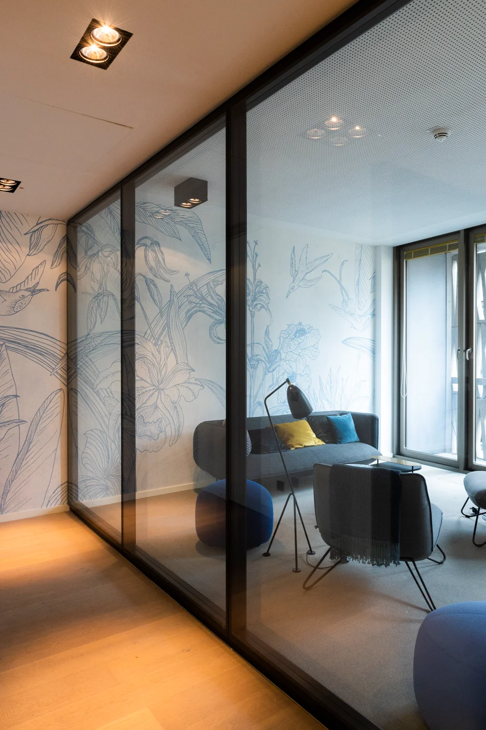 Glass-walled lounge with hand-drawn blue botanical wallpaper, sofa and floor lamp, Frankfurt am Main & Munich — Digital+, corporate photography by Janina Laszlo