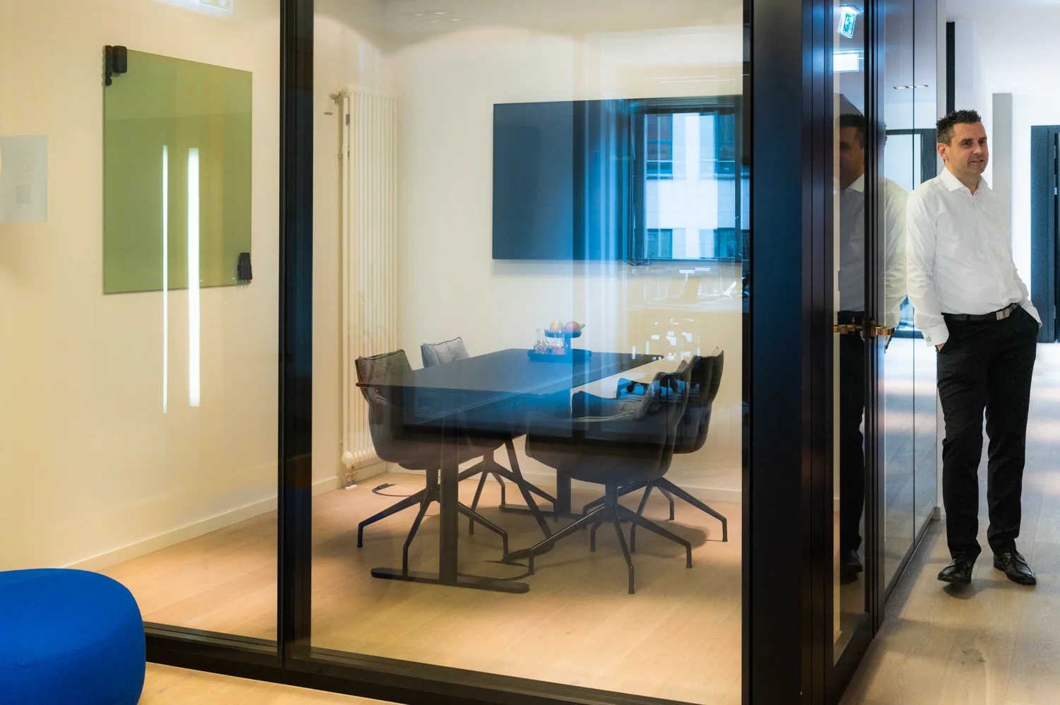 Executive in a white shirt leaning beside a glass meeting room with a dark table, Frankfurt am Main & Munich — Digital+, corporate photography by Janina Laszlo