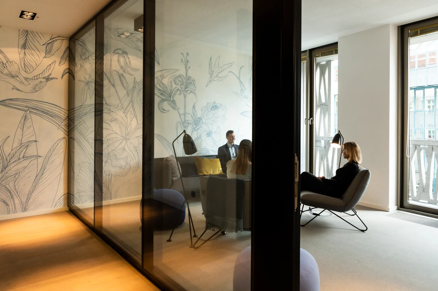 Three colleagues meeting in the lounge with botanical wallpaper, seen through a glass wall, Frankfurt am Main & Munich — Digital+, corporate photography by Janina Laszlo