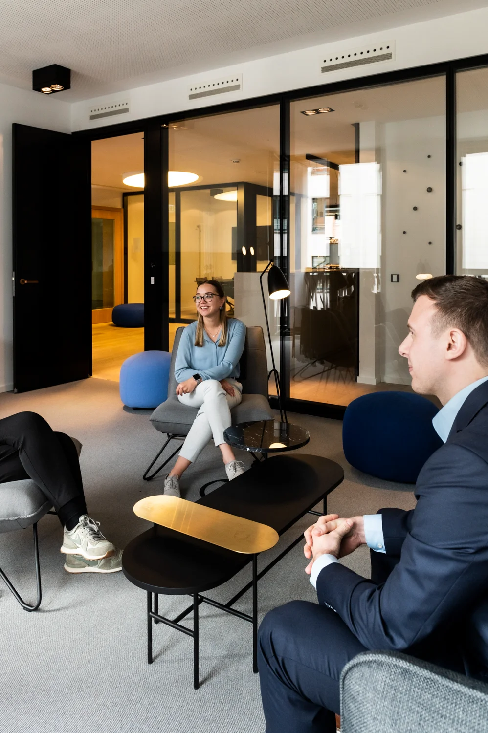 Colleagues in conversation in the lounge with blue poufs and a brass-topped coffee table, Frankfurt am Main & Munich — Digital+, corporate photography by Janina Laszlo