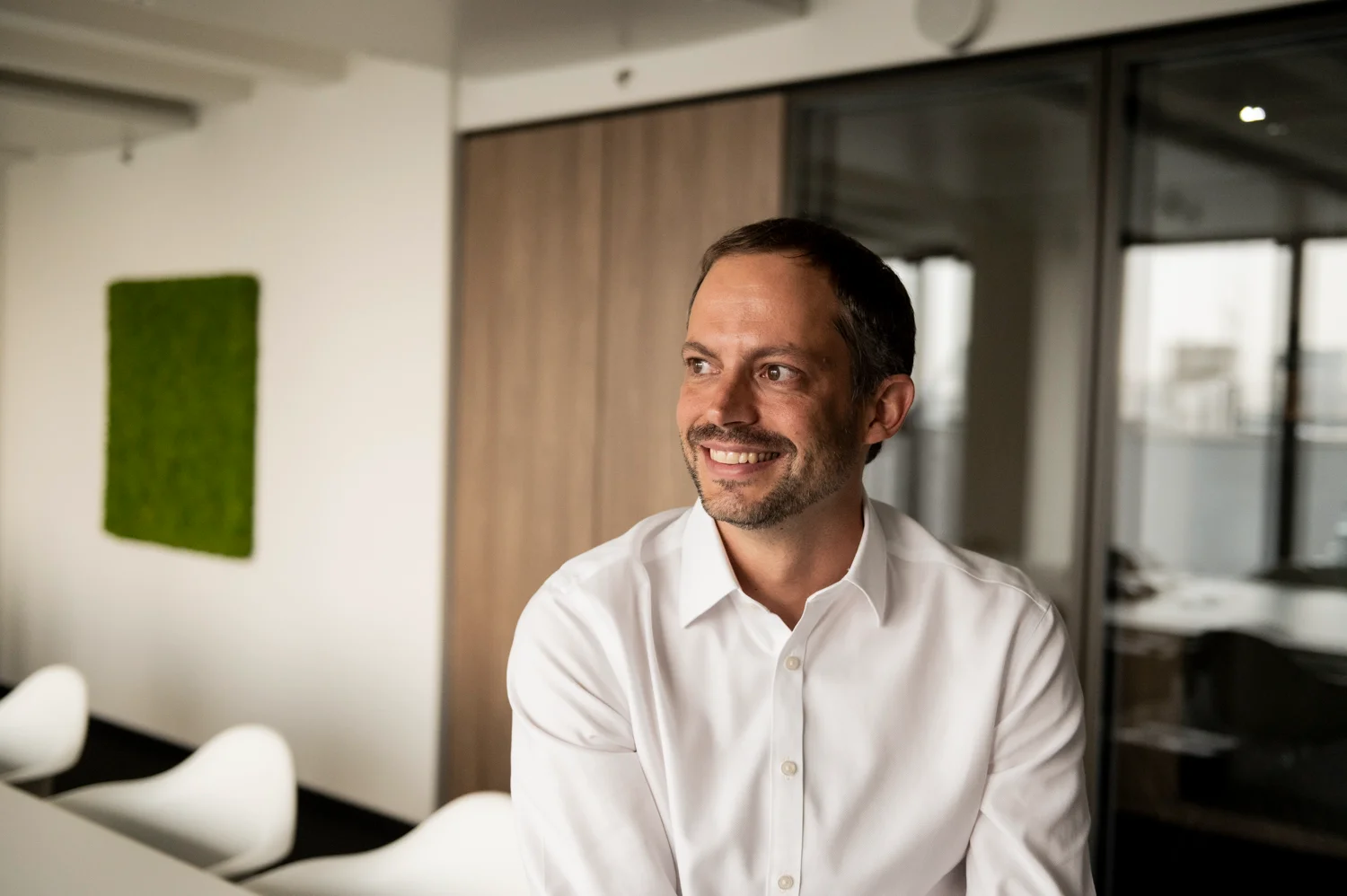 Smiling executive in a white shirt looking out of frame, moss wall in the background, business portrait, Frankfurt am Main & Munich — Digital+, corporate photography by Janina Laszlo