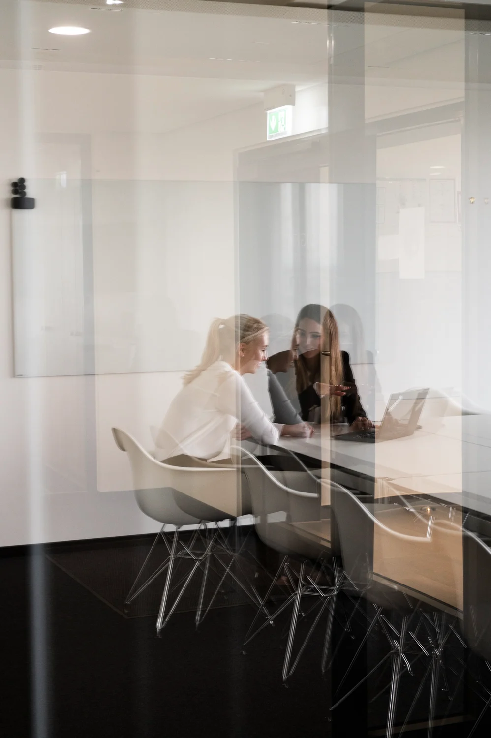 Two colleagues at a laptop in a meeting room, seen through layered glass reflections, Frankfurt am Main — Digital+, corporate photography by Janina Laszlo