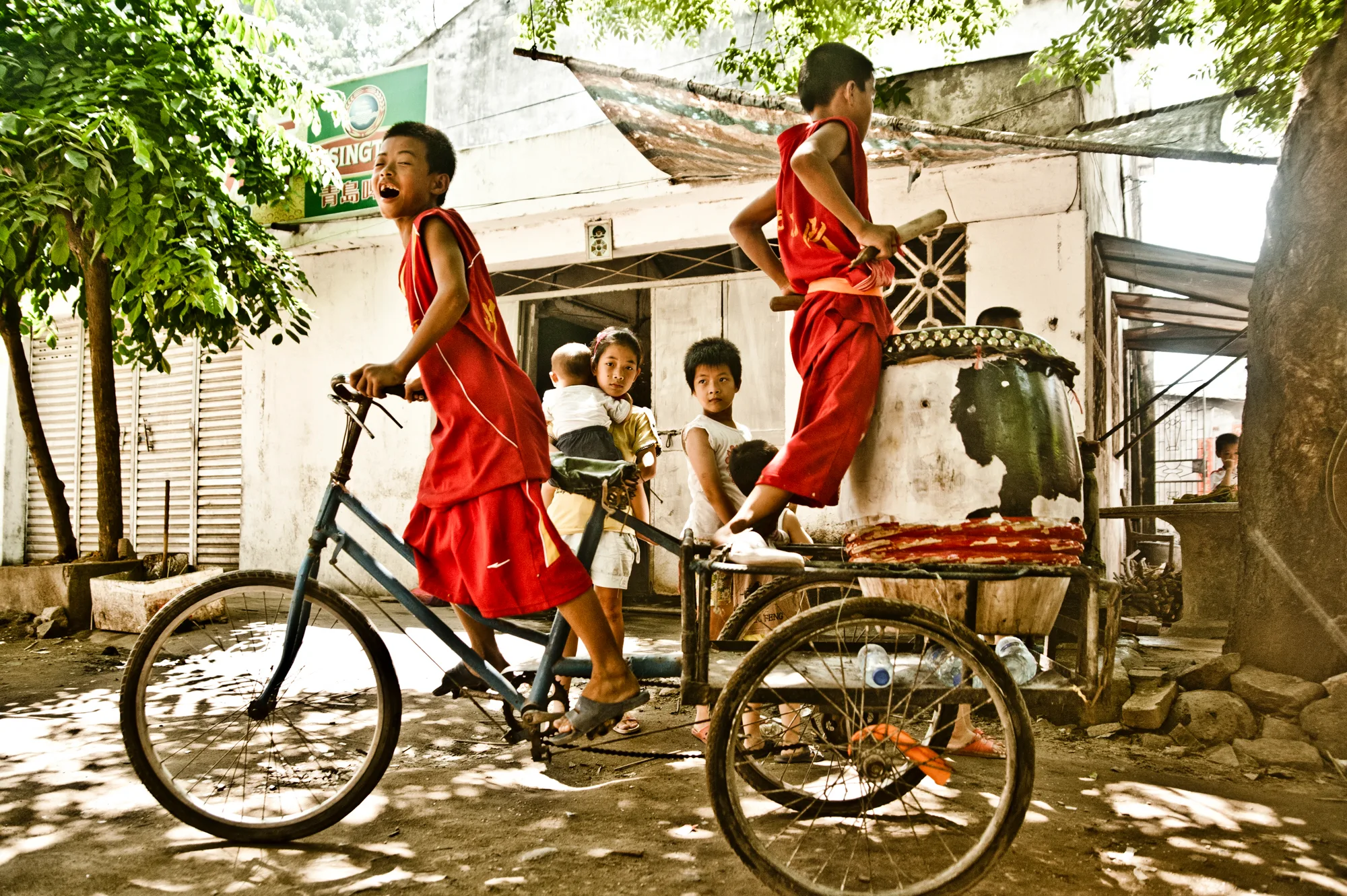 Boy in red standing on a tricycle cart — Dragon Boat Festival Hainan, documentary photography by Janina Laszlo
