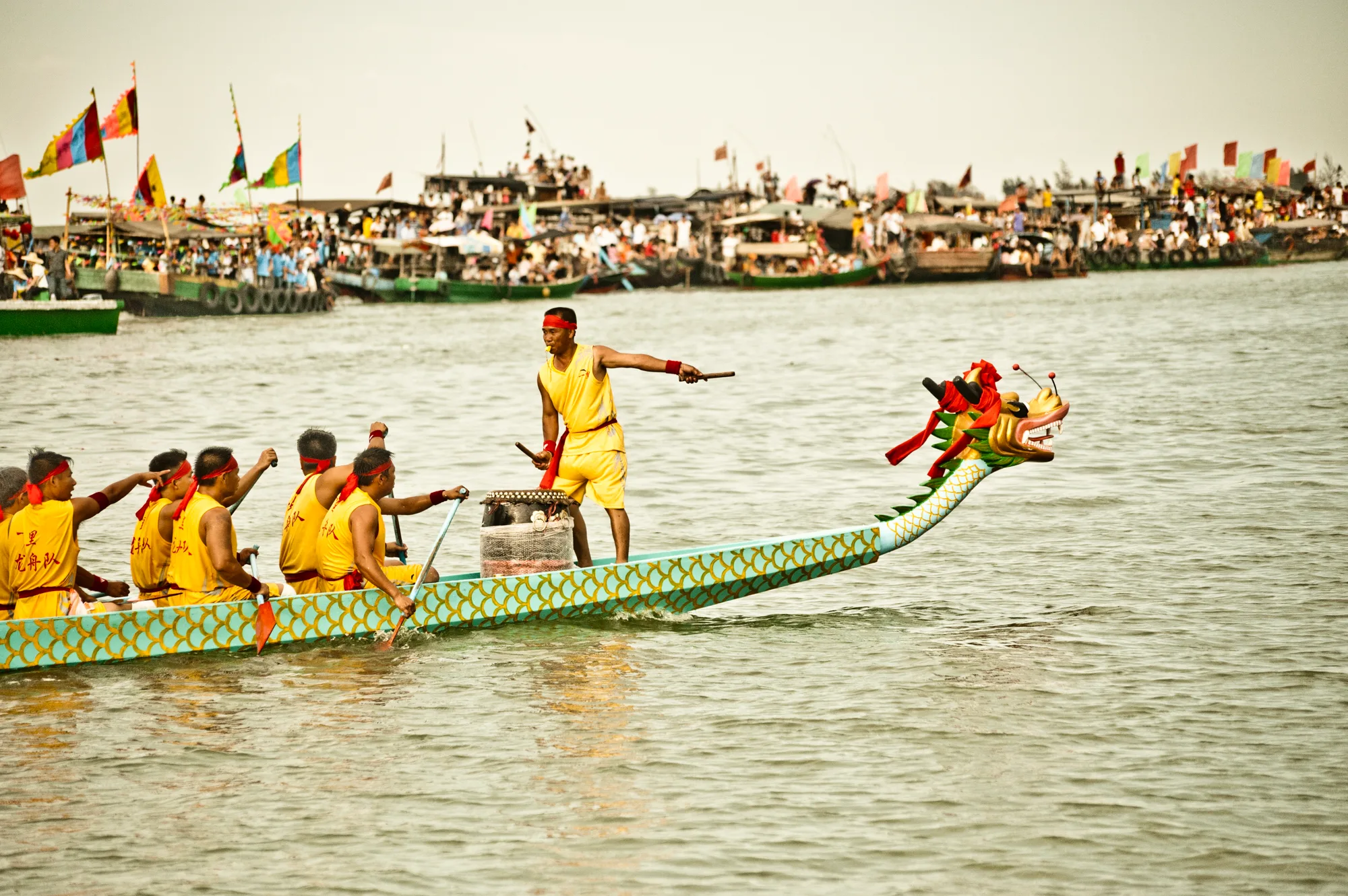 Drummer and rowers in yellow powering a dragon boat — Dragon Boat Festival Hainan, documentary photography by Janina Laszlo