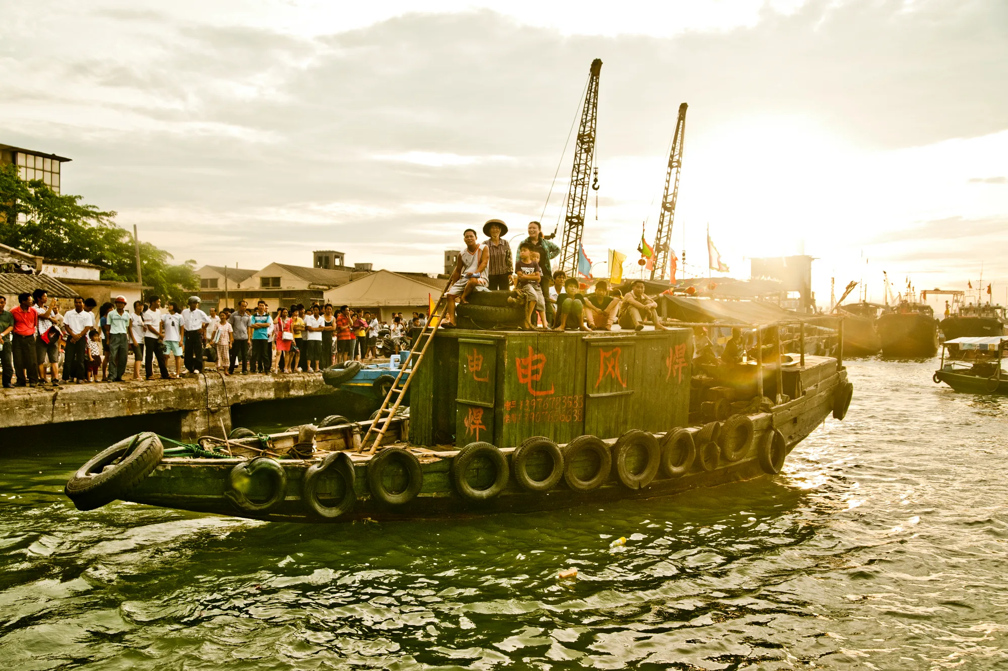 Fishing boat with crowds in golden evening light — Dragon Boat Festival Hainan, documentary photography by Janina Laszlo