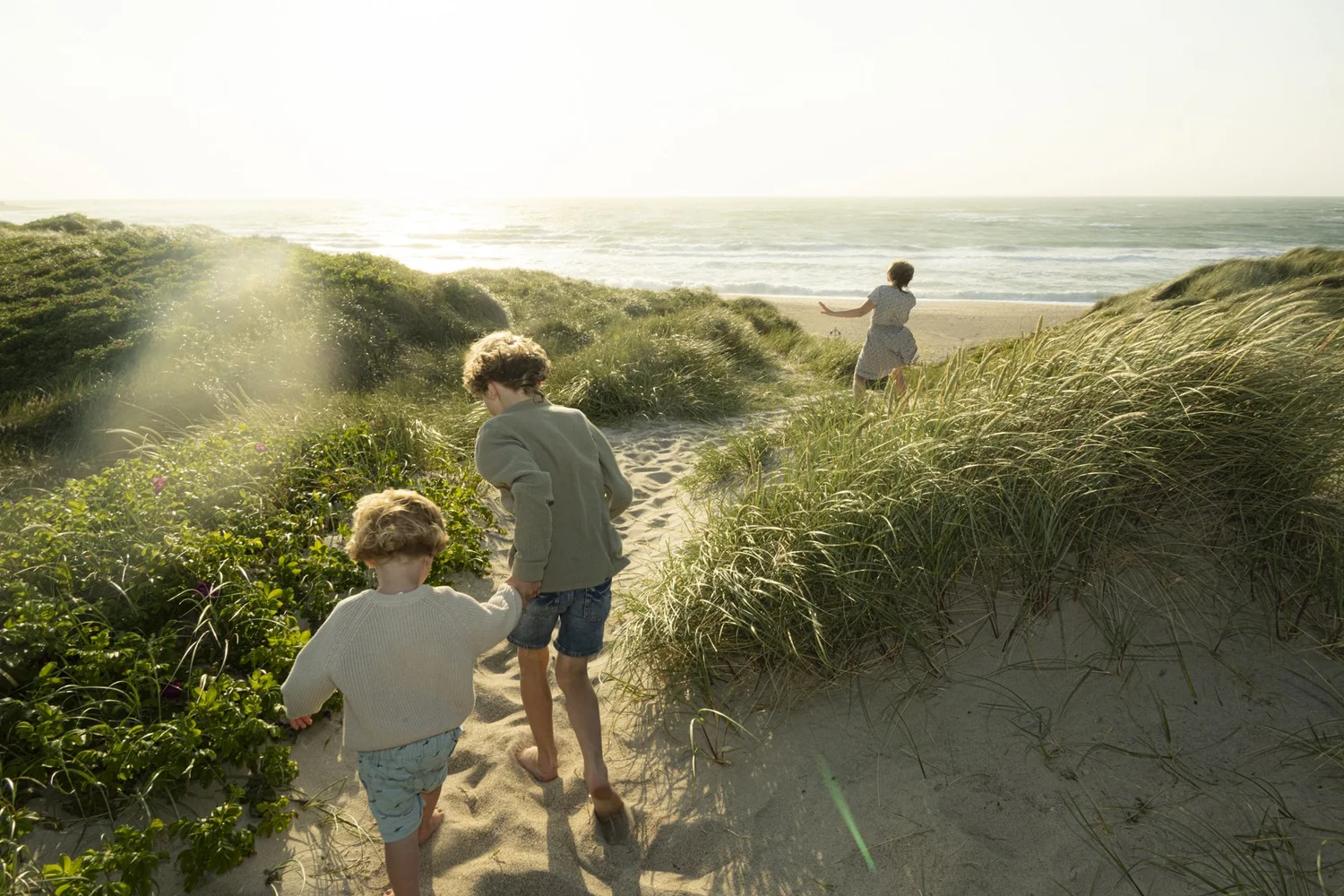 Two children running through the dunes towards the sea in Klitmøller, Denmark, kidswear shoot for Ernsting's family — campaign photography by Janina Laszlo, Munich