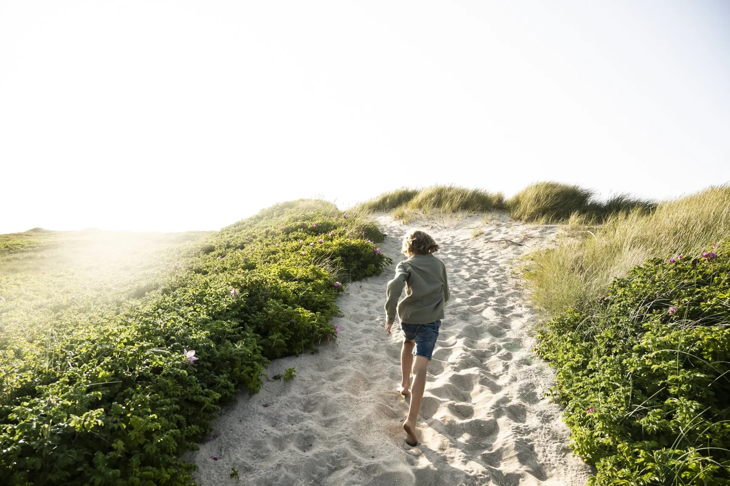 Child walking barefoot along a sandy dune path to the beach, Danish coast, Ernsting's family kids fashion — campaign photography by Janina Laszlo, Munich