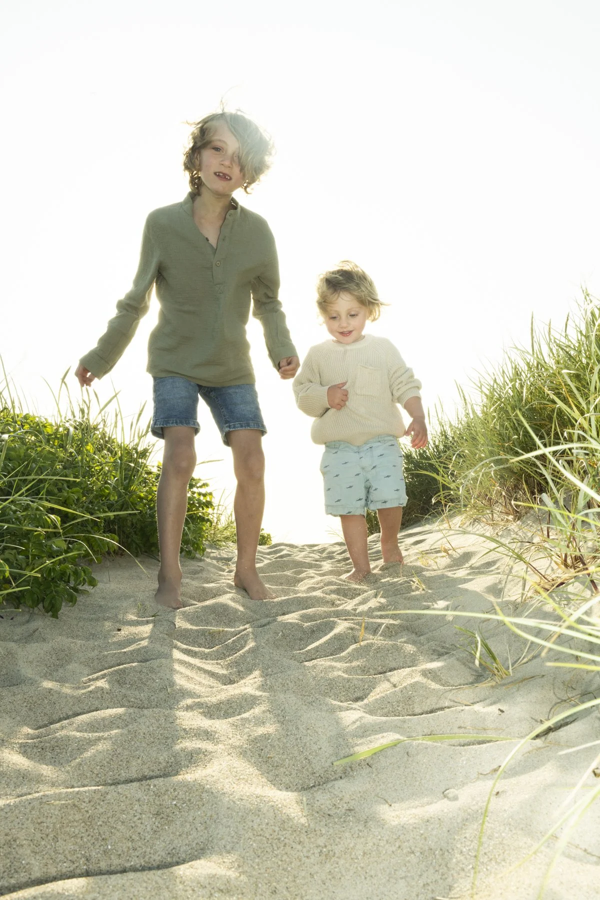 Mother and child walking hand in hand on a dune path in summer light, Ernsting's family, Denmark — campaign photography by Janina Laszlo, Munich