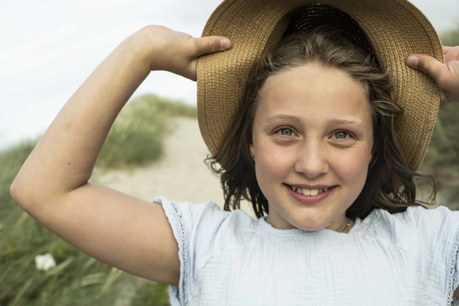 Smiling girl holding on to her straw hat in the wind, children's fashion for Ernsting's family — campaign photography by Janina Laszlo, Munich