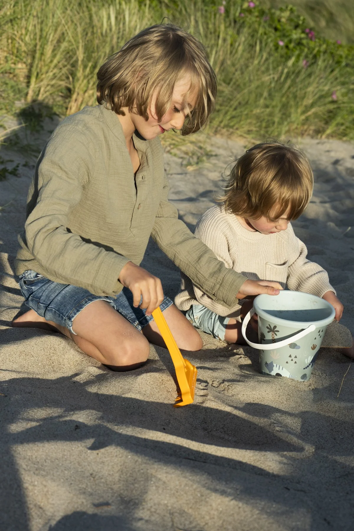 Two children playing with a shovel and bucket in the sand, Ernsting's family kids collection, Denmark — campaign photography by Janina Laszlo, Munich