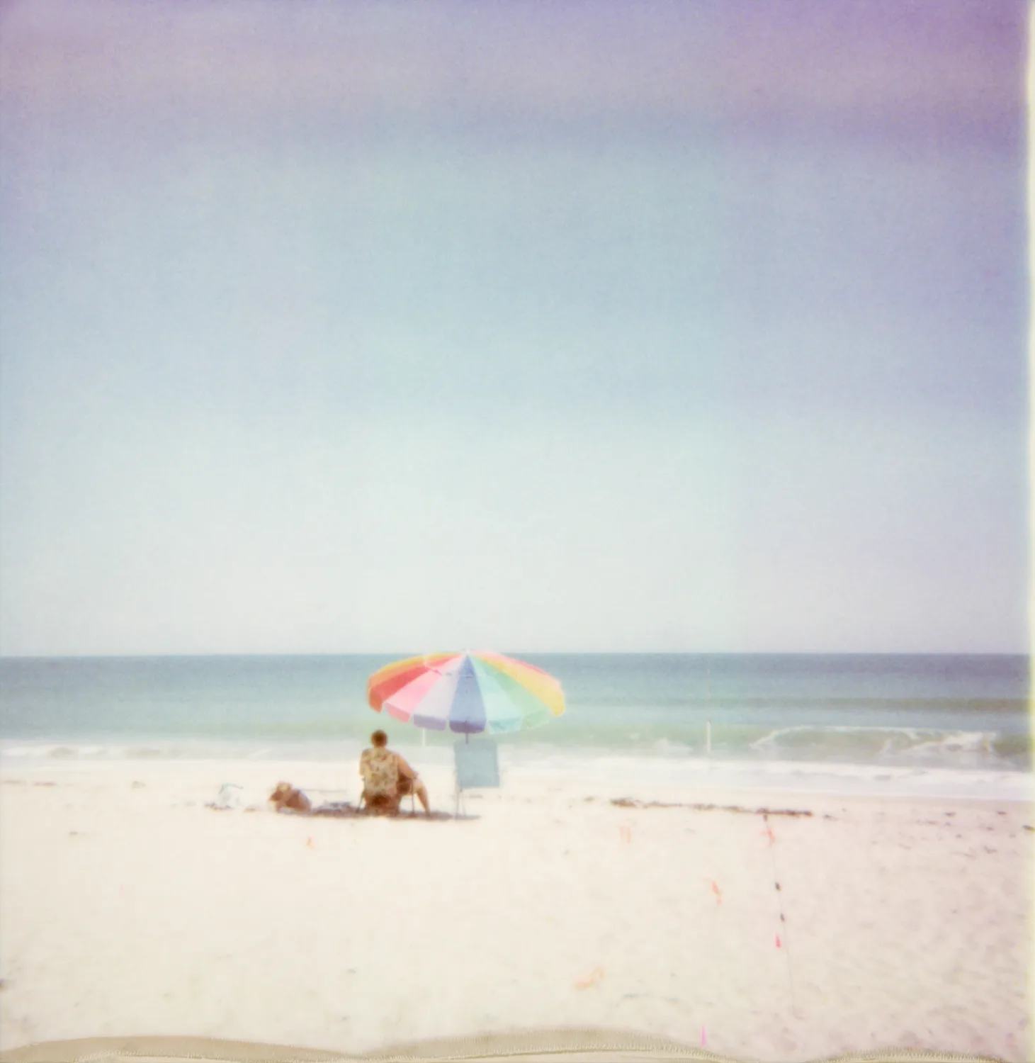 Beach umbrella in rainbow colours on a pale beach — Expired Polaroids in Florida, fine art and analog photography by Janina Laszlo