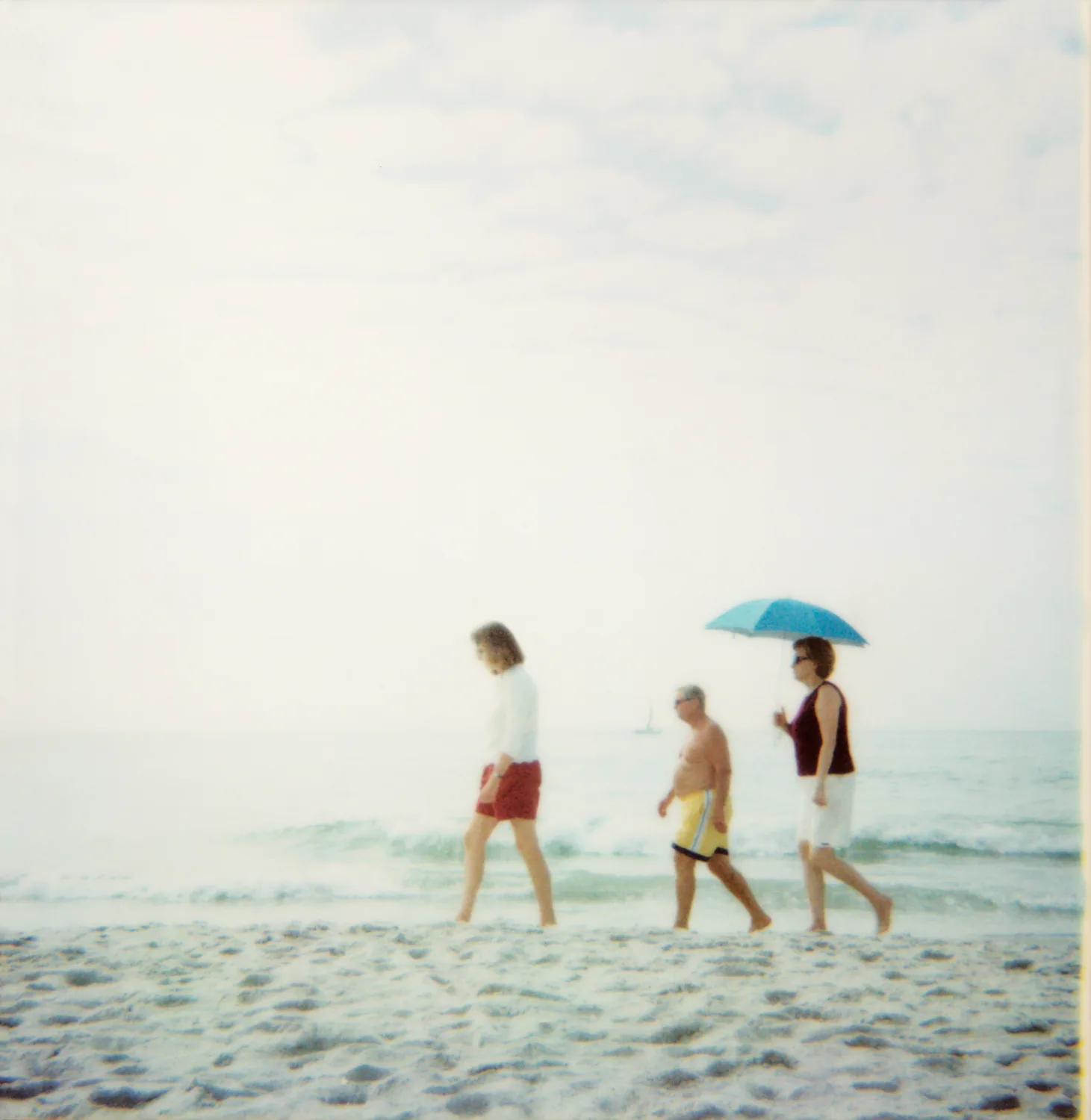 Three people walking along the shoreline, one under a blue umbrella — Expired Polaroids in Florida, fine art and analog photography by Janina Laszlo