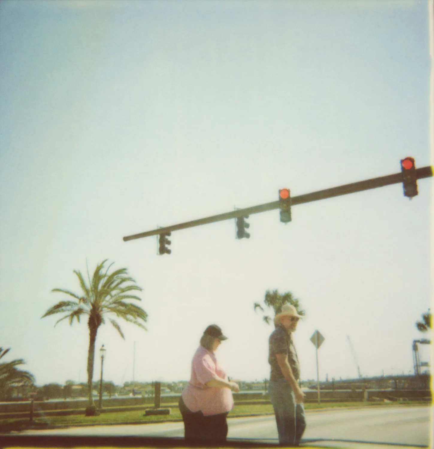 Couple crossing the street beneath red traffic lights and palm trees — Expired Polaroids in Florida, fine art and analog photography by Janina Laszlo