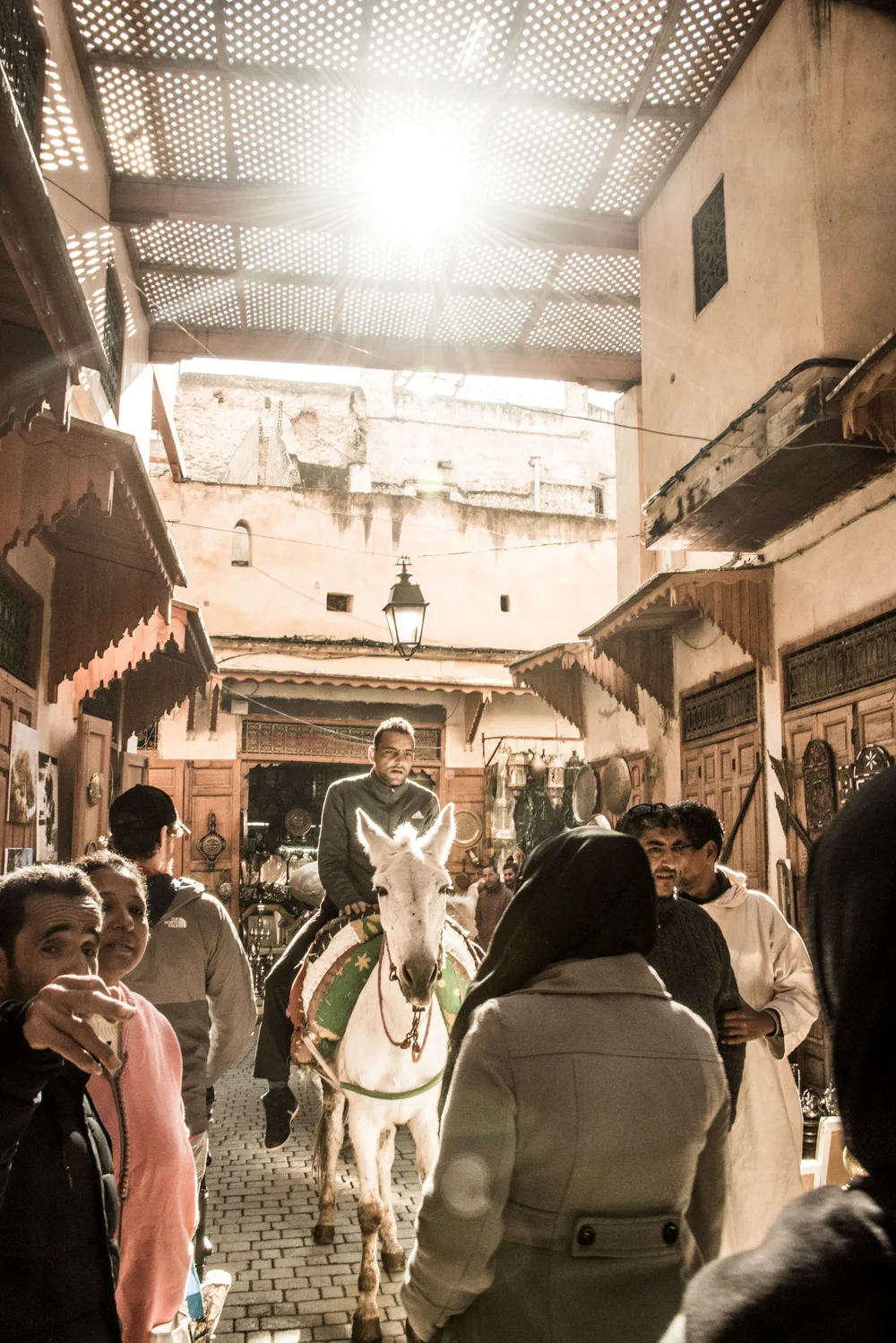 Man riding a white mule through a sunlit covered souk, Fez medina — Fez, street and travel photography by Janina Laszlo
