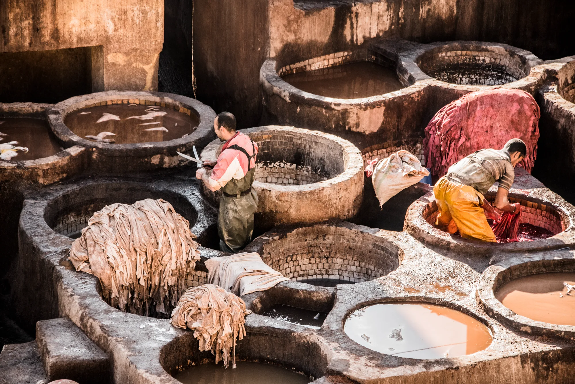 Two tanners working hides in red dye and clay vats, Chouara Tannery, Fez — Fez, street and travel photography by Janina Laszlo