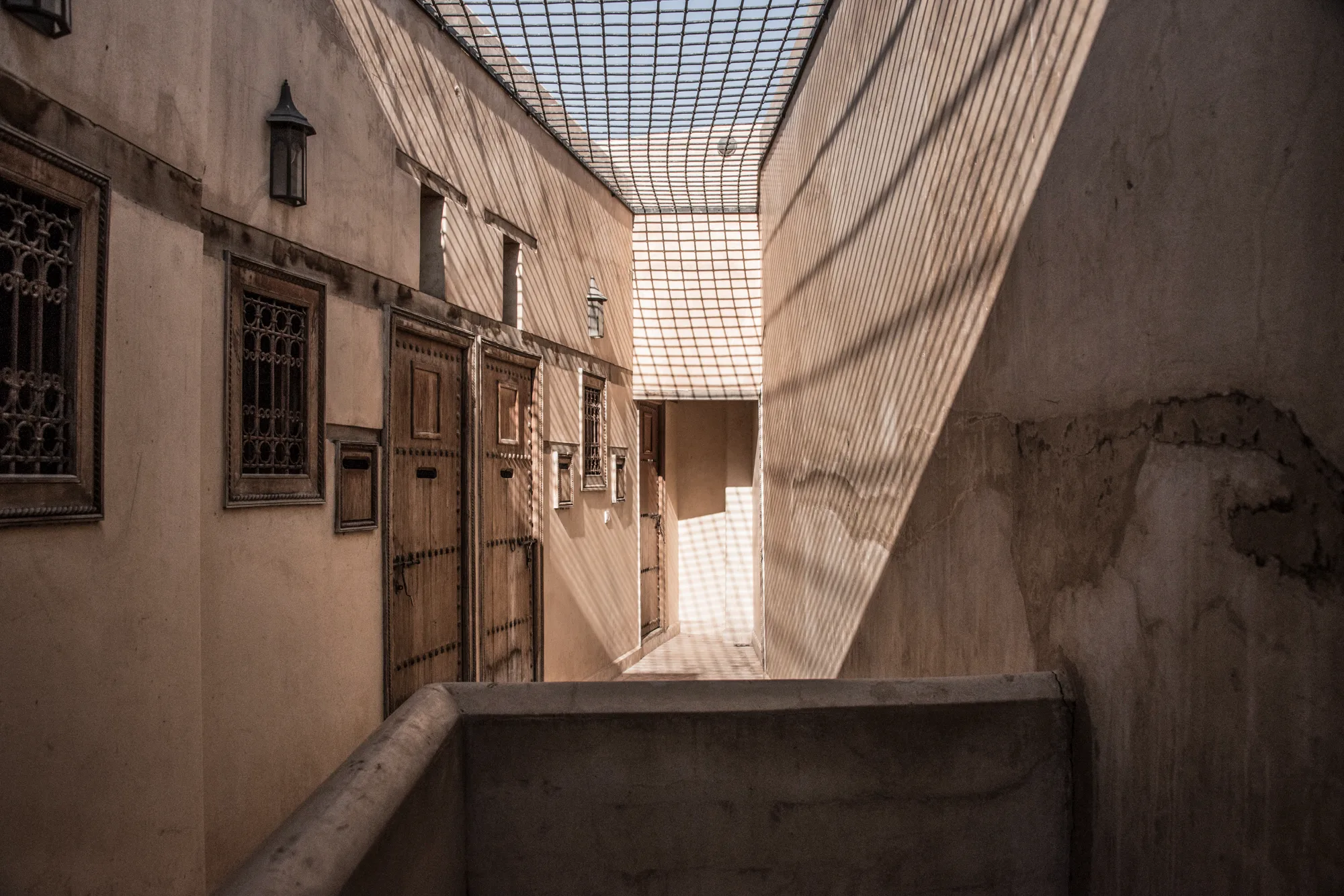 Grid shadows of a rooftop screen on a riad corridor with carved wooden doors, Fez — Fez, street and travel photography by Janina Laszlo