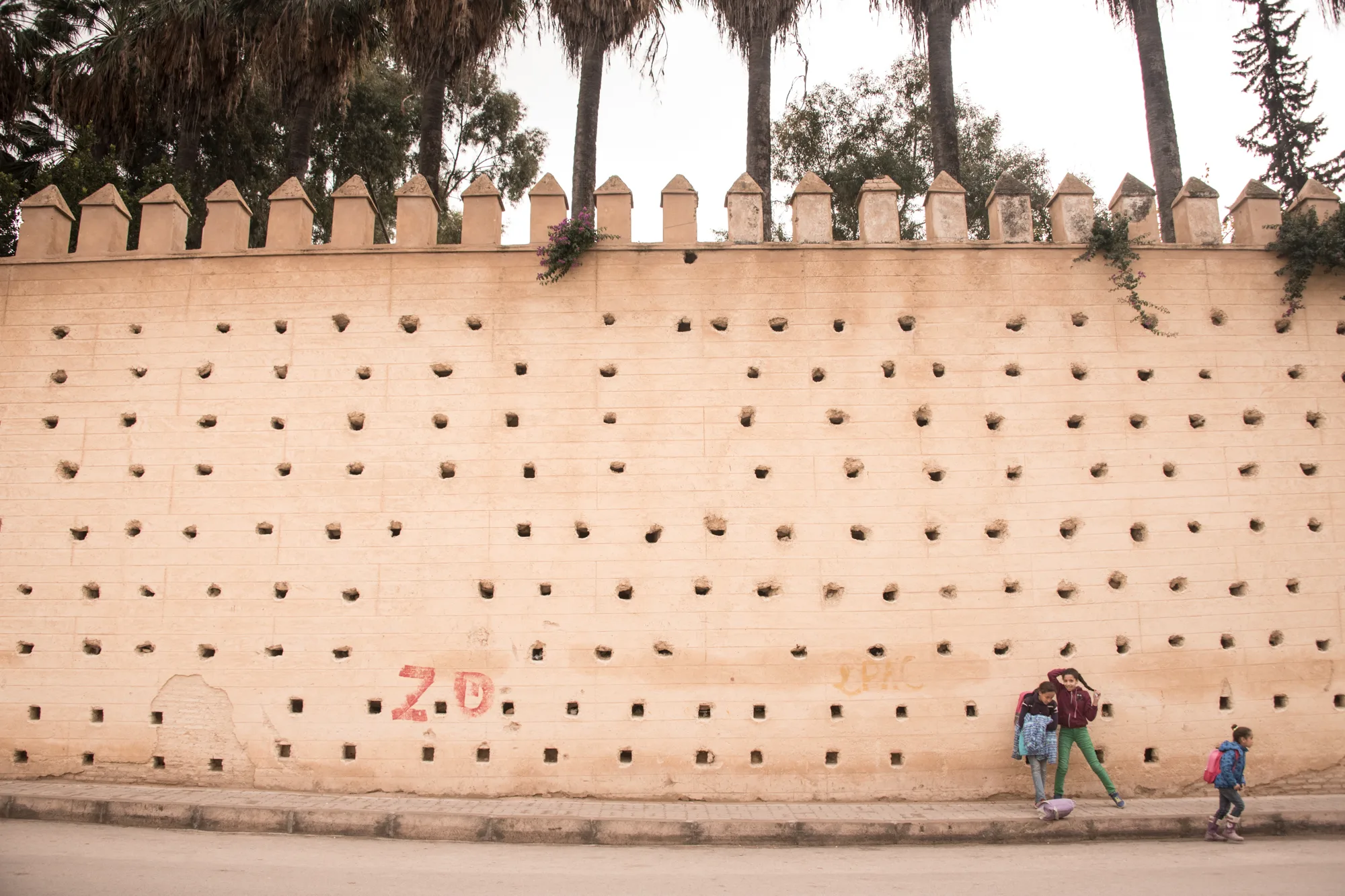 Girls by a crenellated city wall with rows of putlog holes, Fez — Fez, street and travel photography by Janina Laszlo