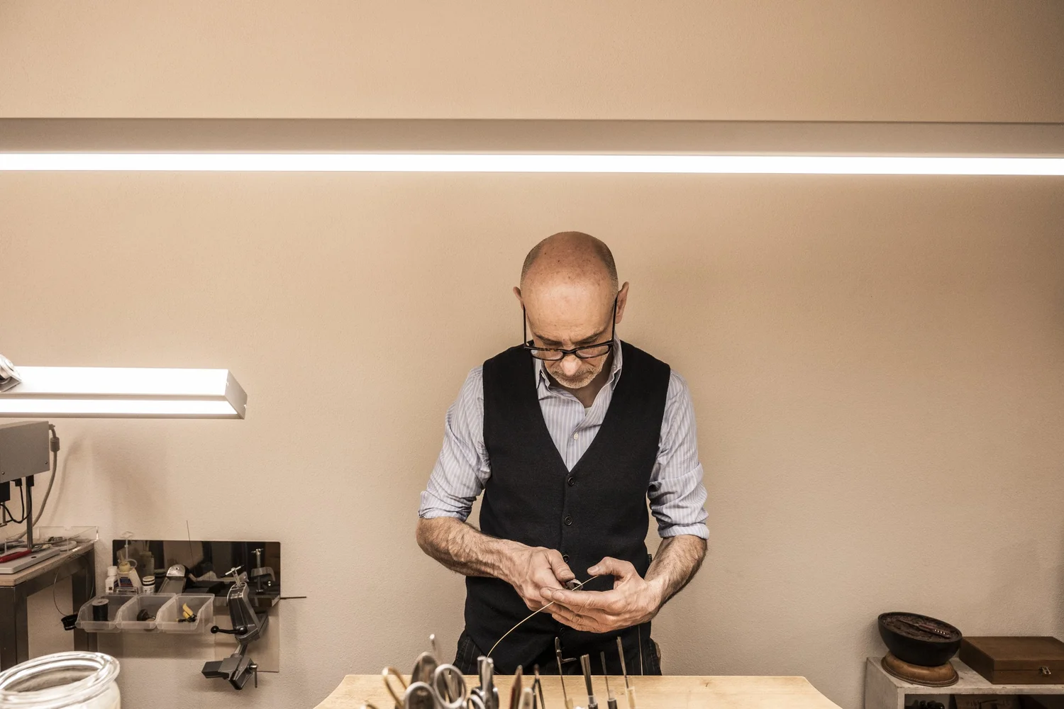 Goldsmith at his workbench under fluorescent light, wide view of the workshop — reportage by Janina Laszlo, photographer in Munich