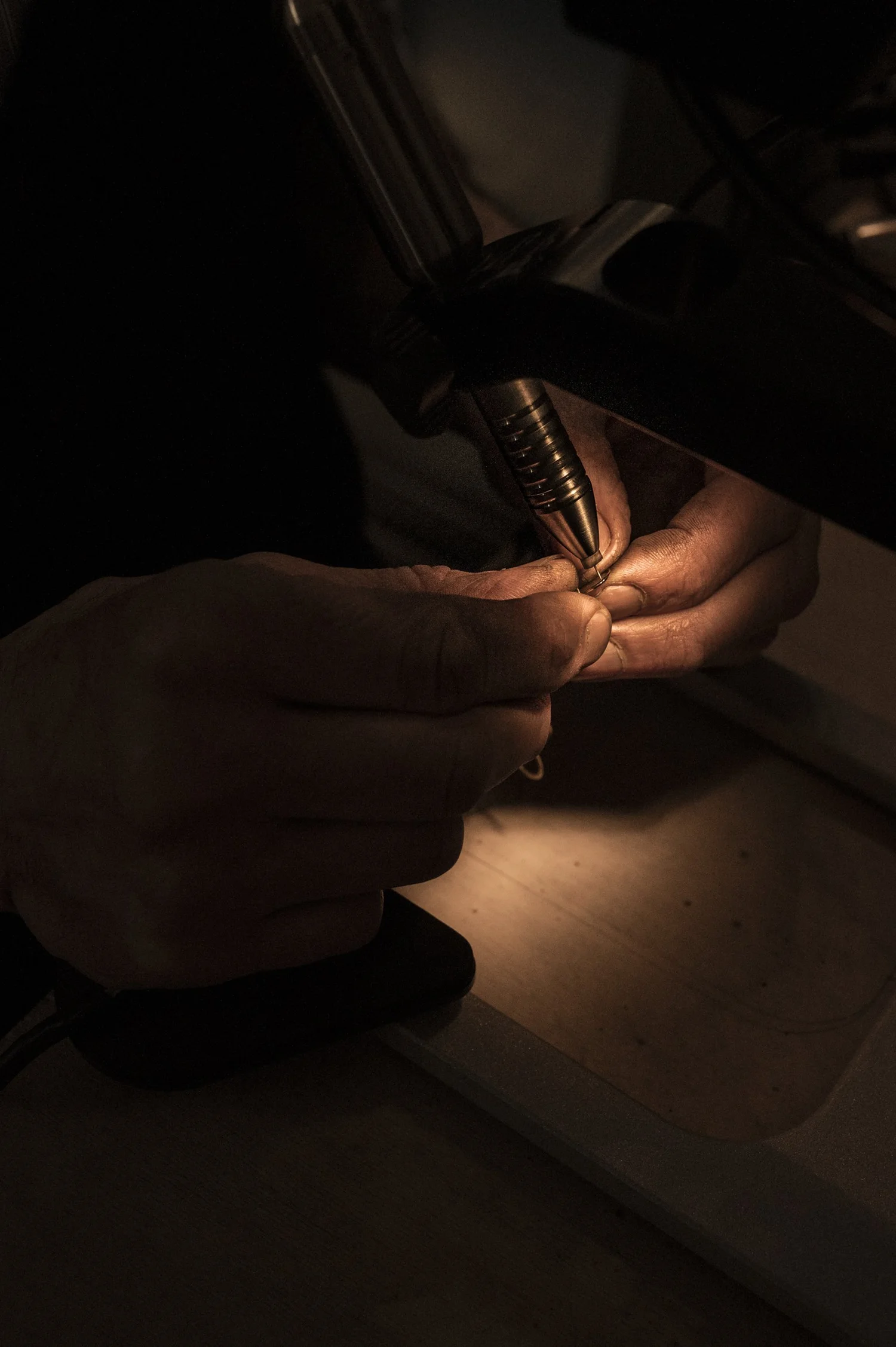 Hands holding a gold ring under a single lamp in the dark, goldsmith detail — reportage by Janina Laszlo, photographer in Munich