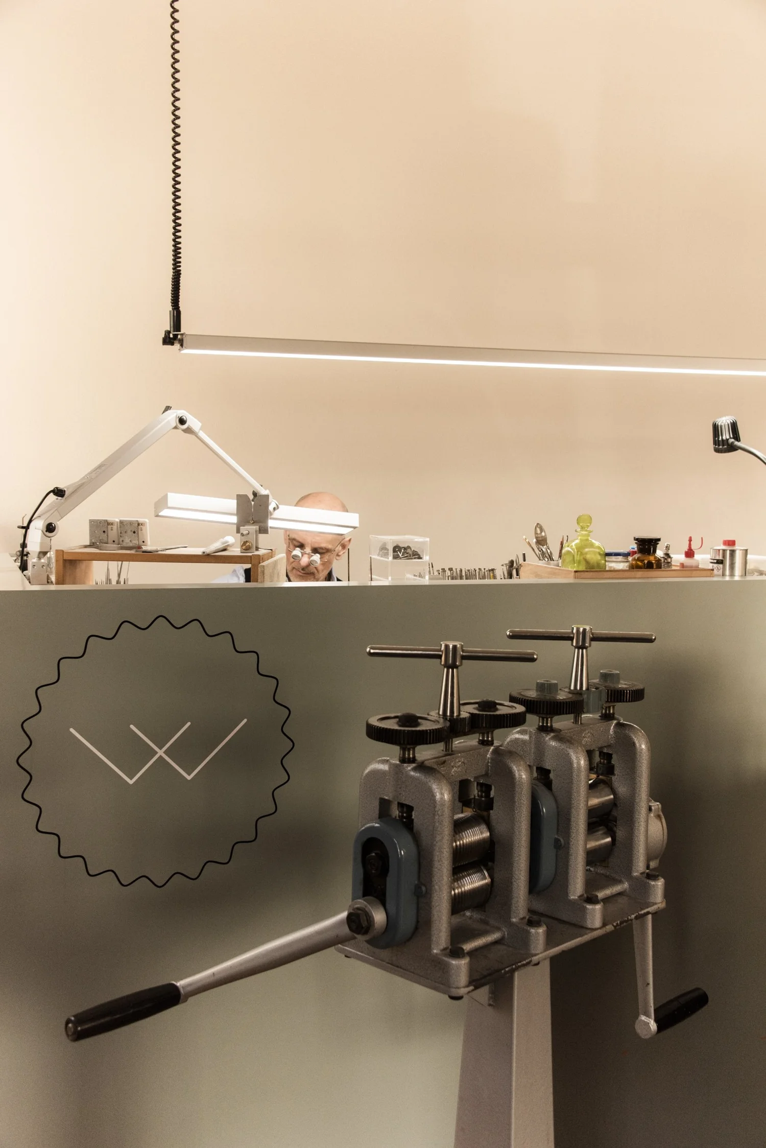 Hand-cranked rolling mill below the Weickmann logo and a hanging workshop lamp — reportage by Janina Laszlo, photographer in Munich