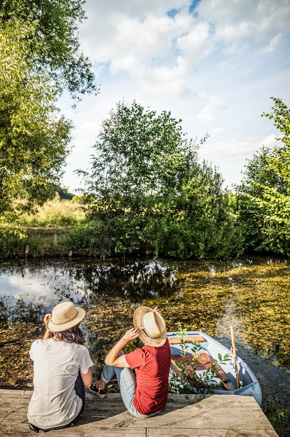 Two women in straw hats seen from behind on a jetty by a pond, taking a break from cycling the Hop Route in Bavaria — tourism campaign photography by German photographer Janina Laszlo